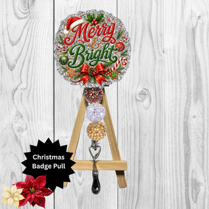 A Christmas-themed badge pull sign displayed on a small wooden easel against a white wood plank background. The circular sign reads “Merry & Bright” in red and green lettering with holiday decorations including a Santa hat, holly, candy canes, pinecones, and ornaments.