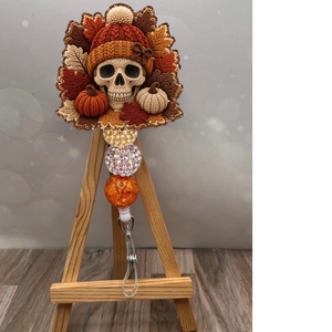 Fall Crochet Skull Badge Pull showcasing a colorful skull design with autumn leaves and pumpkins on a wooden stand.