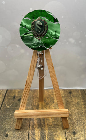 Slytherin badge pull with glitter displayed on a wooden easel, featuring green and black marble design.