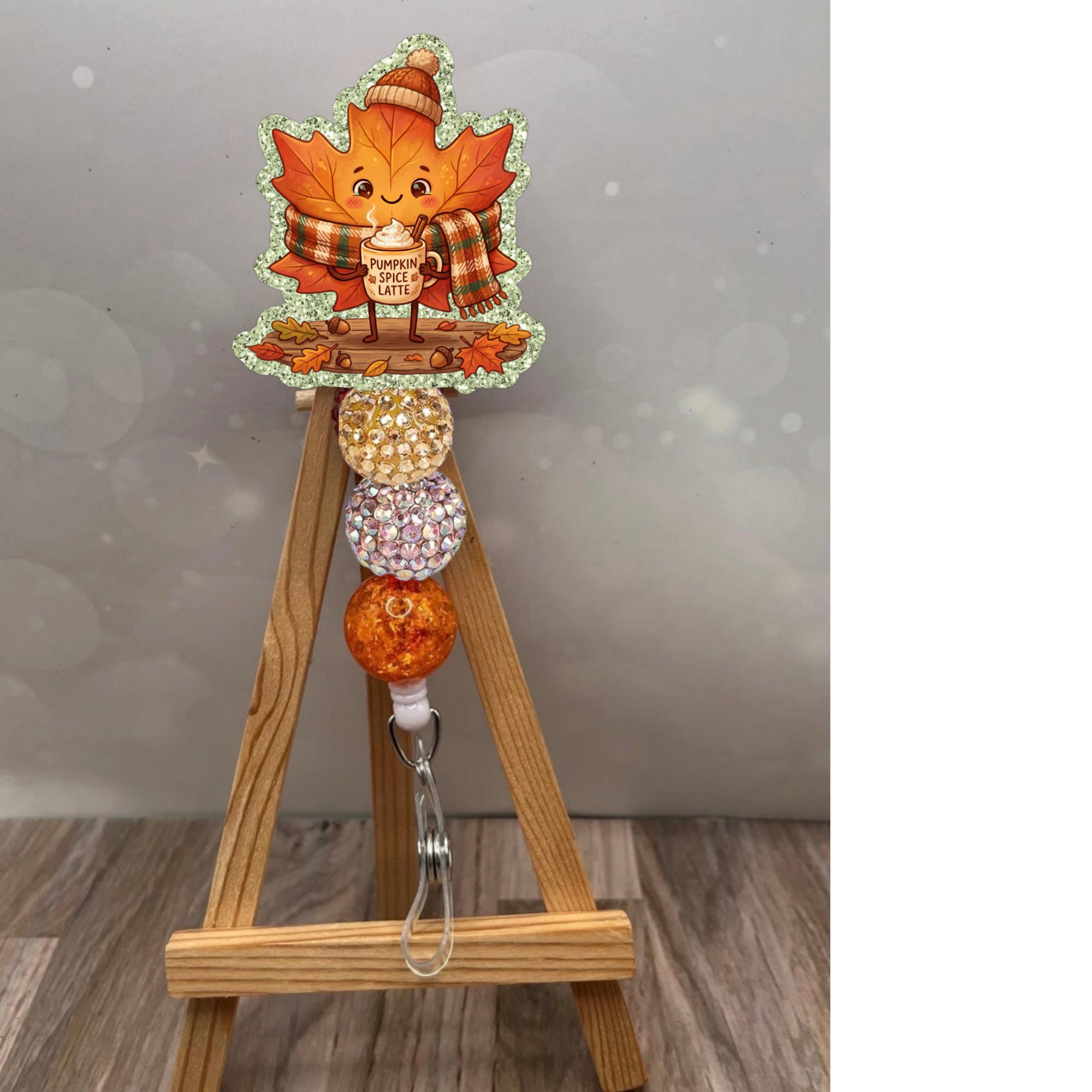 fall leaf badge reel featuring a cute cartoon leaf character holding a pumpkin spice latte, adorned with sparkling beads.