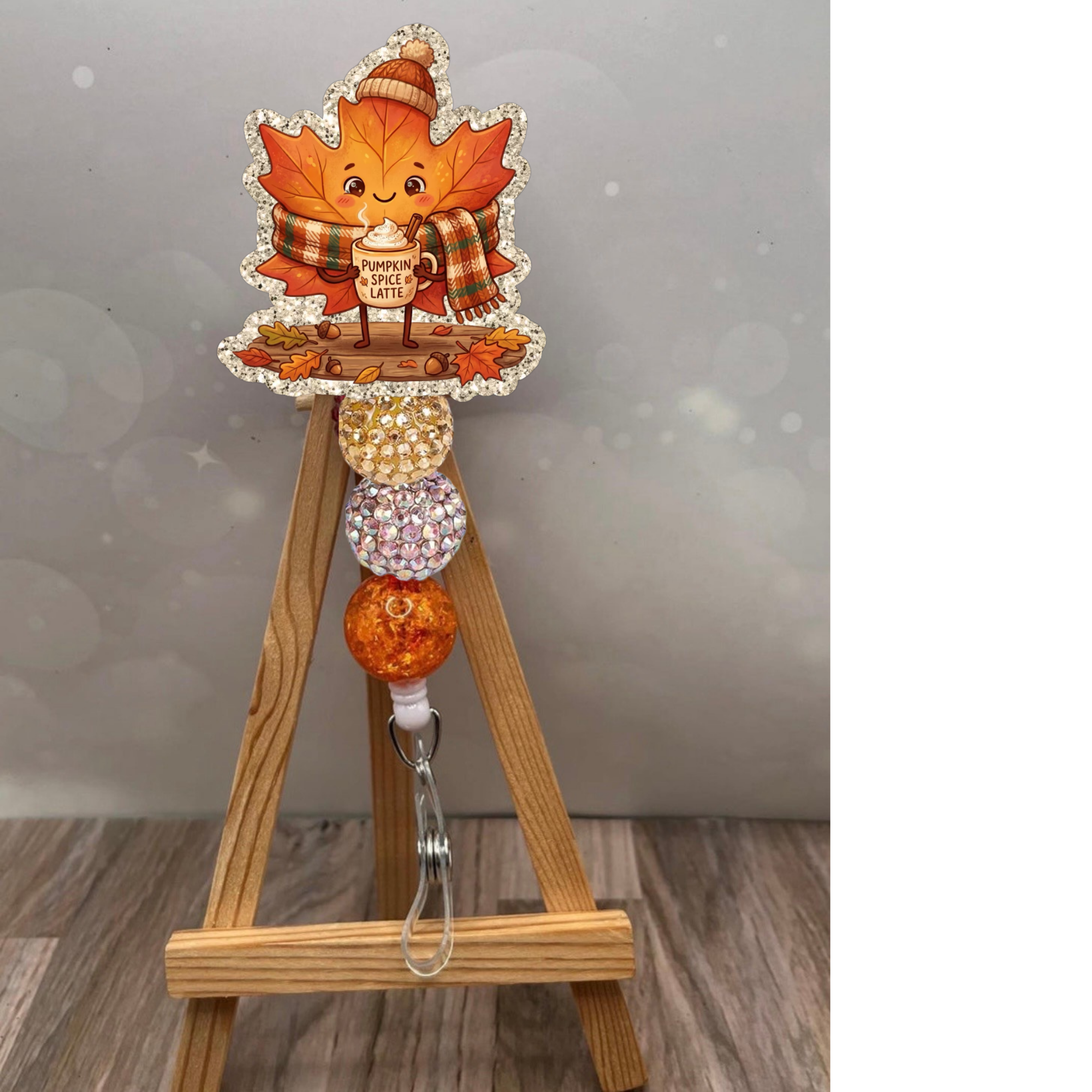 Fall leaf badge reel featuring a cute character holding a pumpkin spice latte with glittery beads, perfect for autumn.