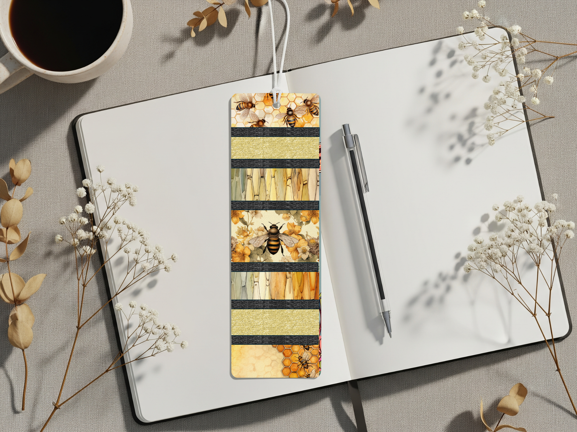 Honeybee aluminum bookmarks with vibrant designs displayed on a notebook and surrounded by dried flowers.