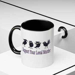 A white ceramic mug with a black handle and black interior, printed with four black birds and the phrase 'Support Your Local Murder' in dark purple text. The mug is shown on a clean white geometric background with a black handle-shaped shadow or prop on the right.