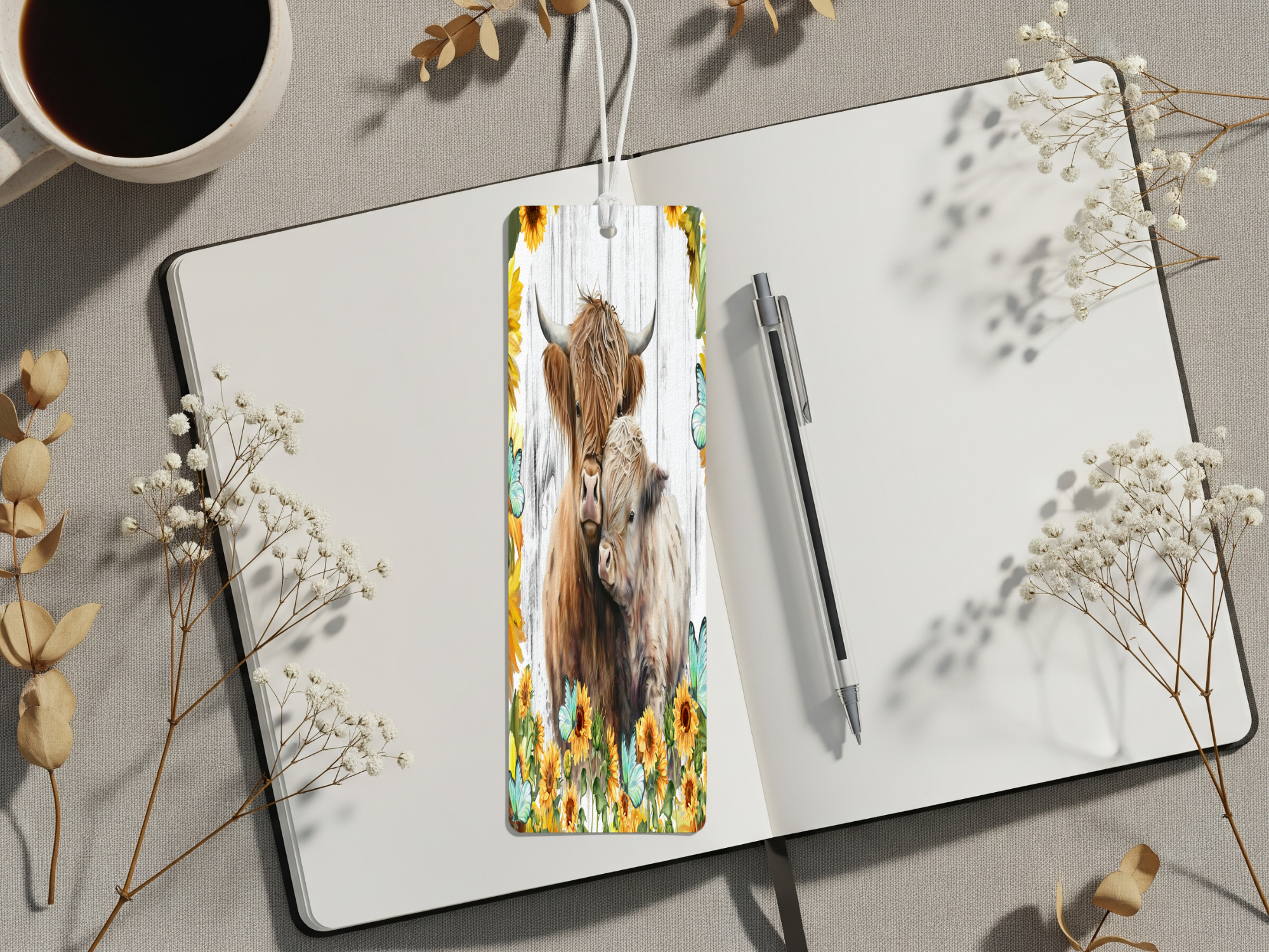 Aluminum highland cow metal bookmarks displayed on a notebook with flowers and a coffee cup.