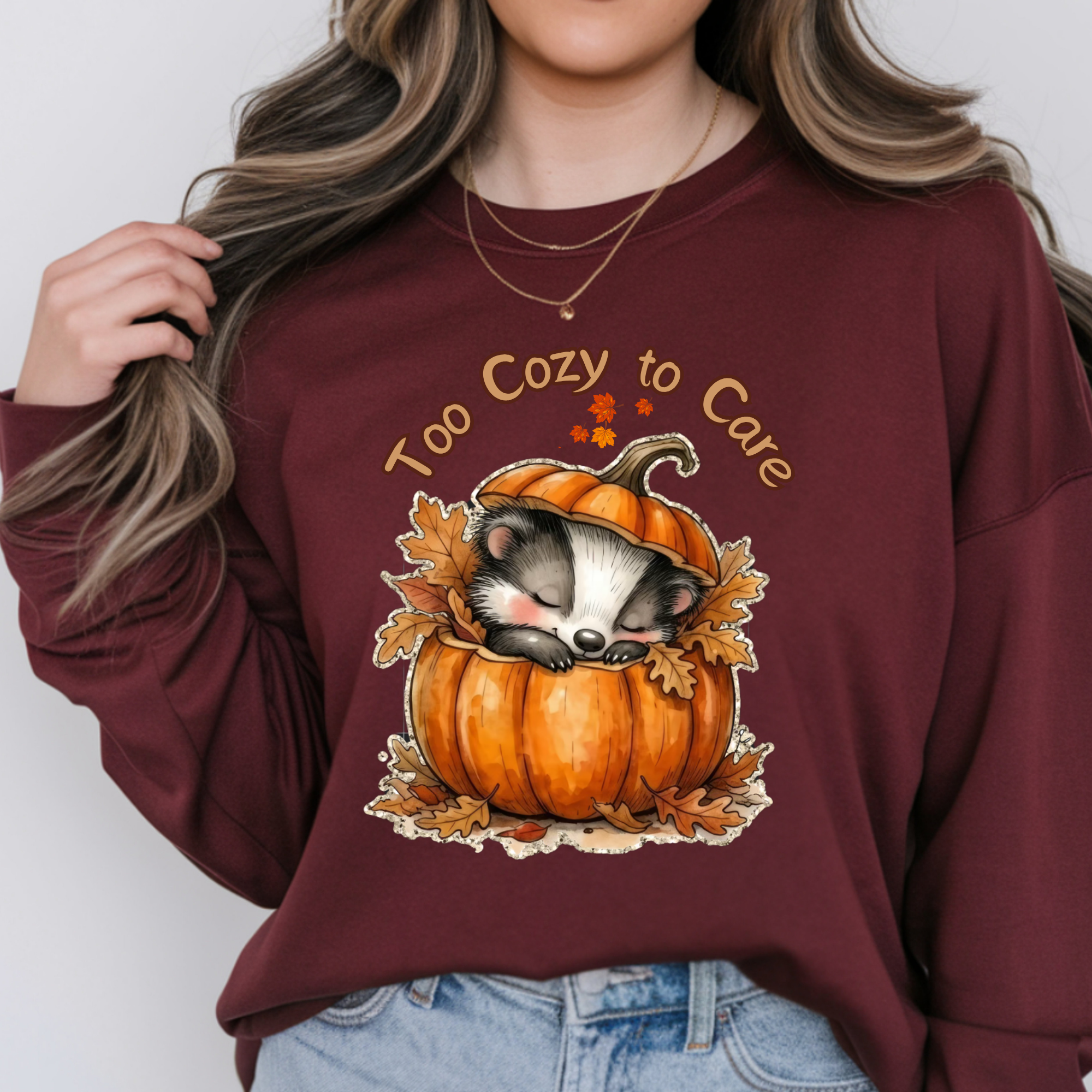 Woman wearing a cozy long sleeve graphic tee featuring a sleeping raccoon in a pumpkin design.