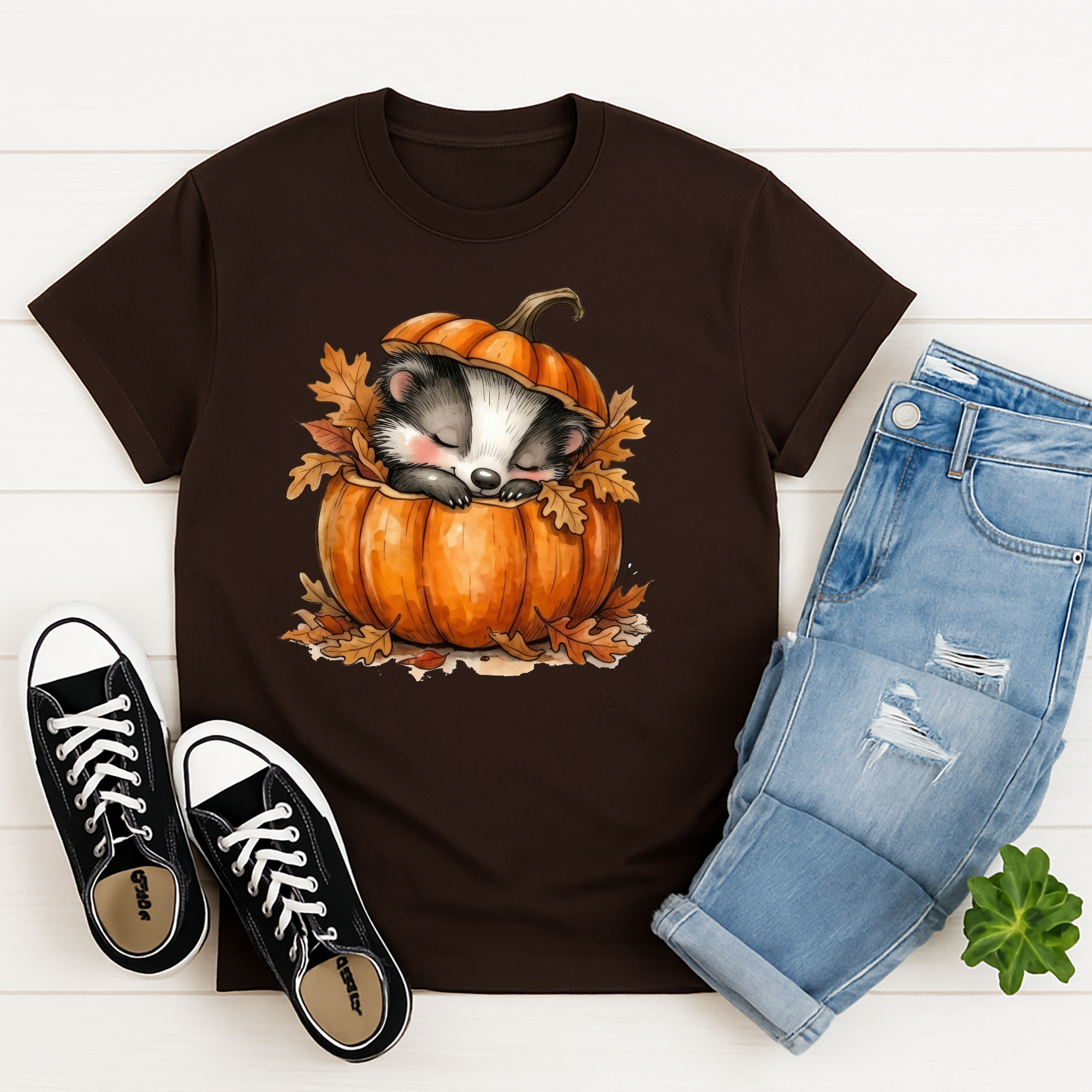 Cozy graphic tee featuring a cute badger sleeping in a pumpkin surrounded by autumn leaves, perfect for casual wear.