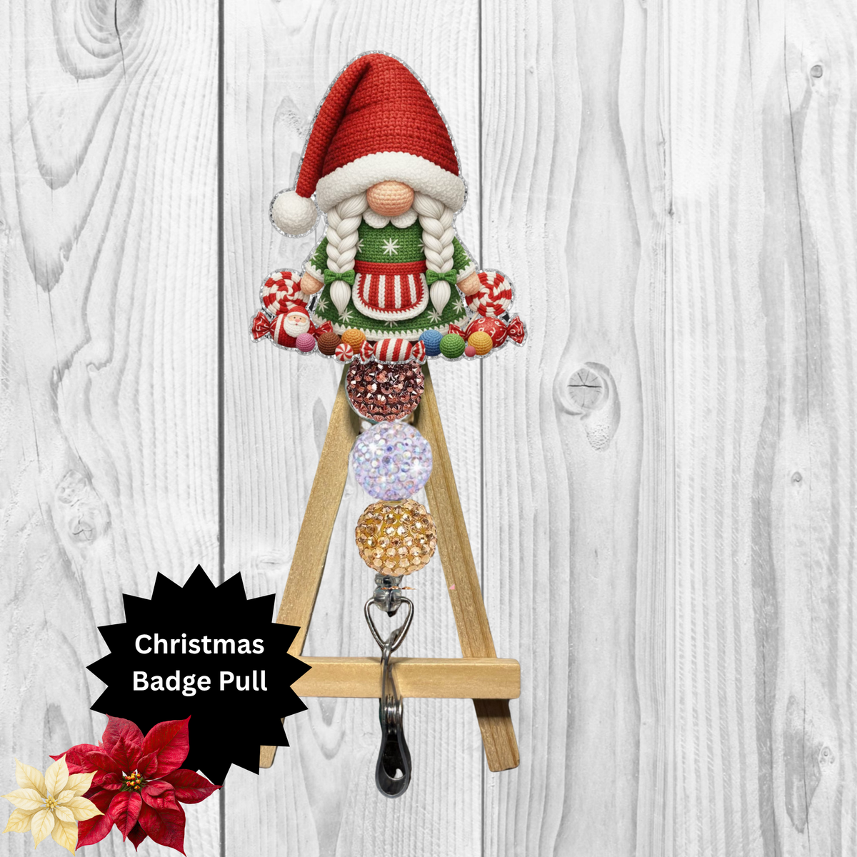 A Christmas-themed wooden A-frame badge pull hook with a festive gnome figure at the top, colorful hanging badges, and a black metal clip. The product is shown against a white wood plank background with a black starburst label reading 'Christmas Badge Pull' and small red/yellow flowers in the lower left corner.