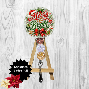 A Christmas-themed badge pull sign with a round 'Merry & Bright' holiday design, a small wooden easel stand, and a black metal clip at the bottom, shown against a white wood plank background with a black starburst label reading 'Christmas Badge Pull'.