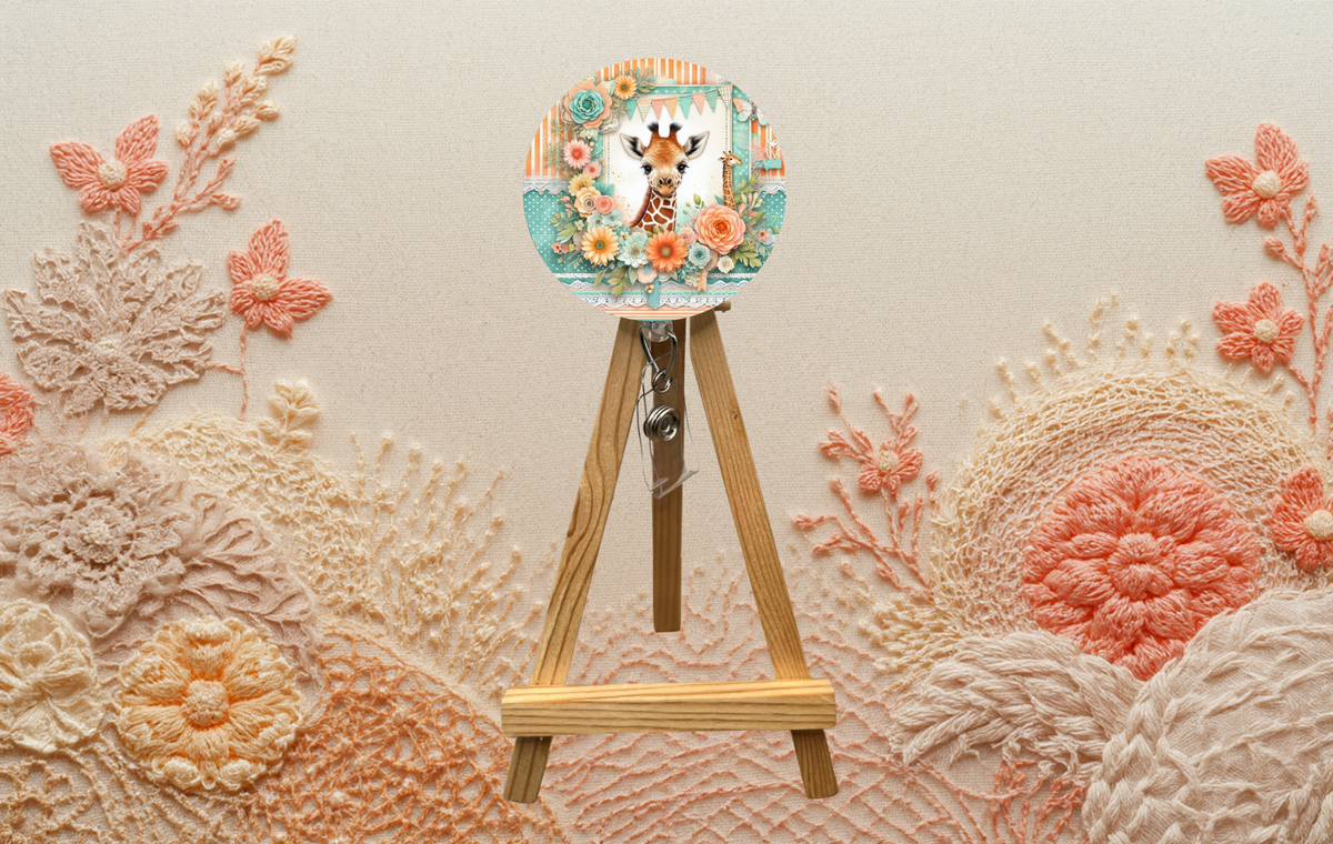 Giraffe badge pulls with glitter displayed on a wooden easel surrounded by floral embroidery.
