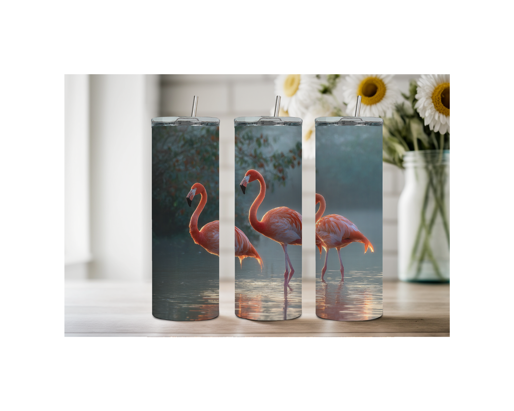 Three pink flamingo stainless steel tumblers with vibrant designs in a sunny, floral setting.