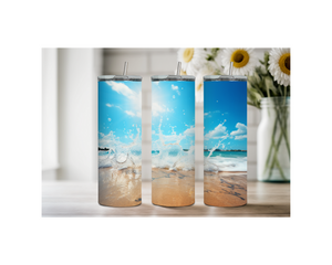 Beach stainless steel tumblers with ocean splash design on a wooden table surrounded by flowers.