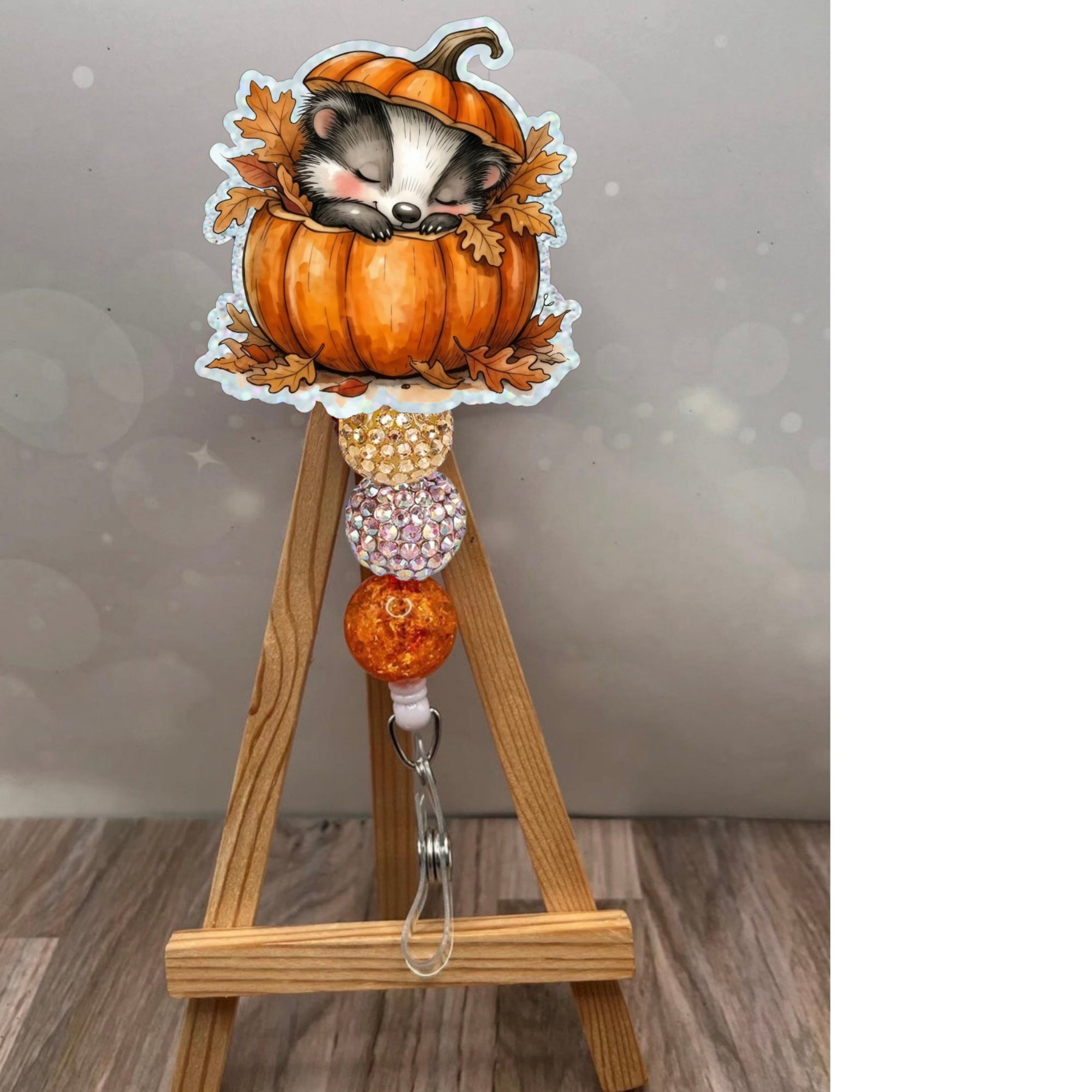 Cozy Badger Badge Reel with cute badger in pumpkin, glittery beads, and nature-inspired design on a wooden easel.