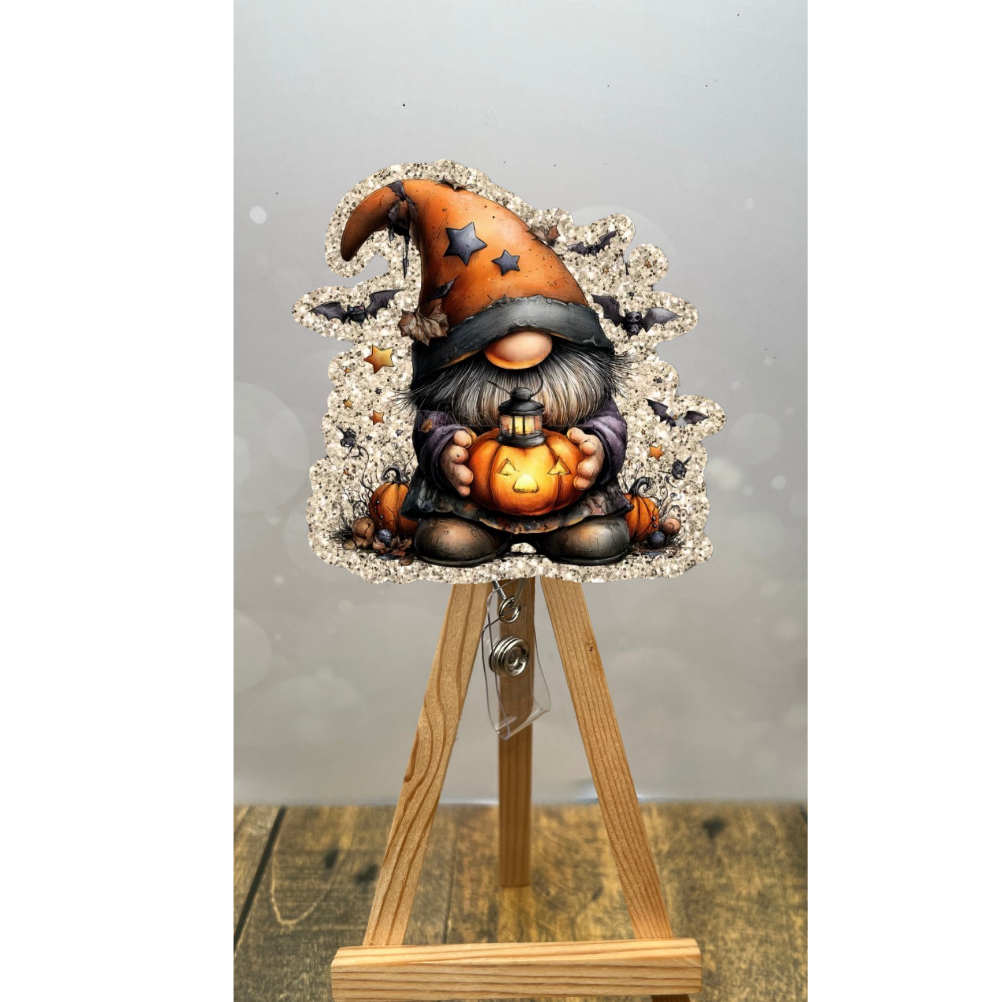 Halloween badge reel gnome holding a pumpkin, whimsical design with glittery champagne background.