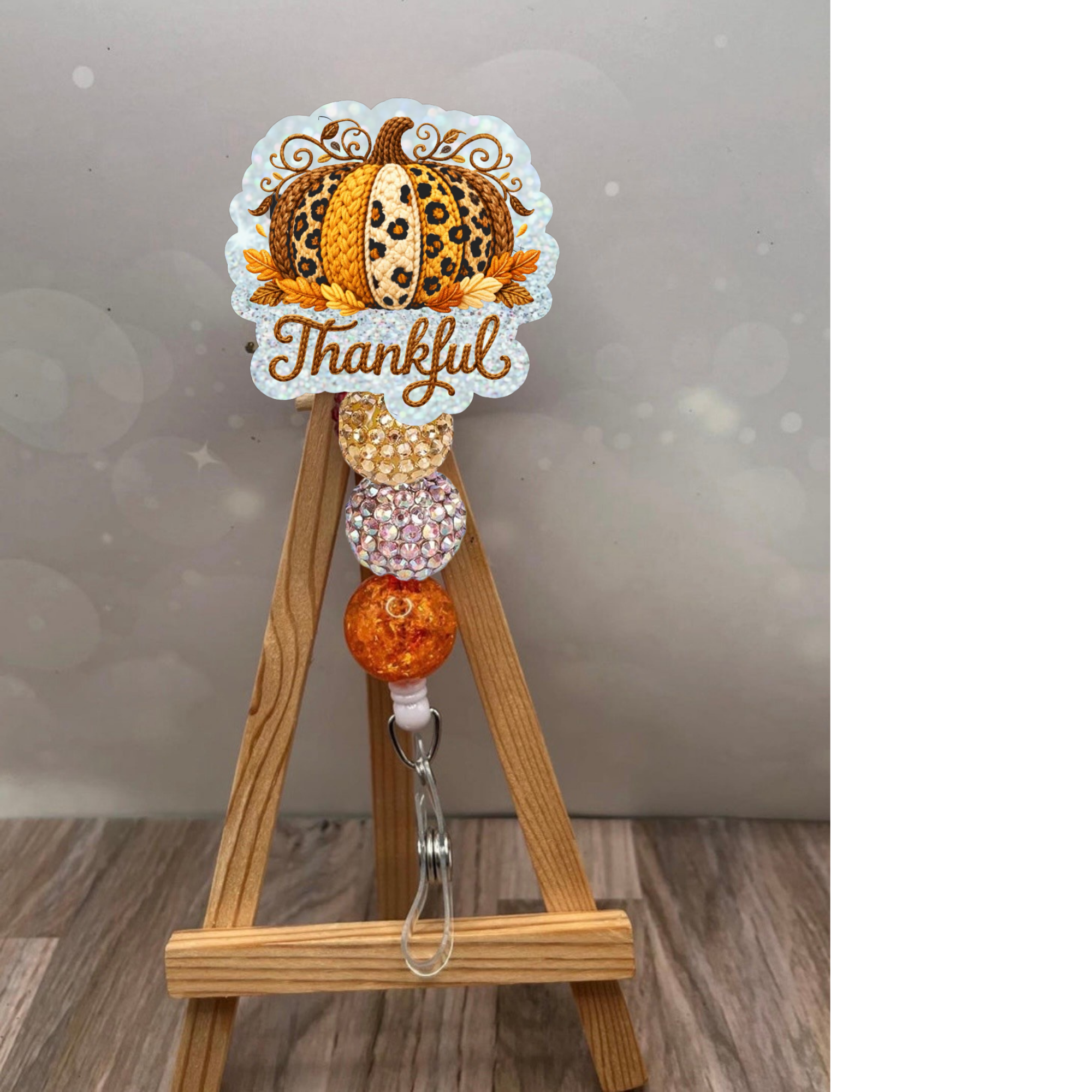 Thankful Crochet Pumpkin Badge Reel with holographic glitter background on wooden easel display.