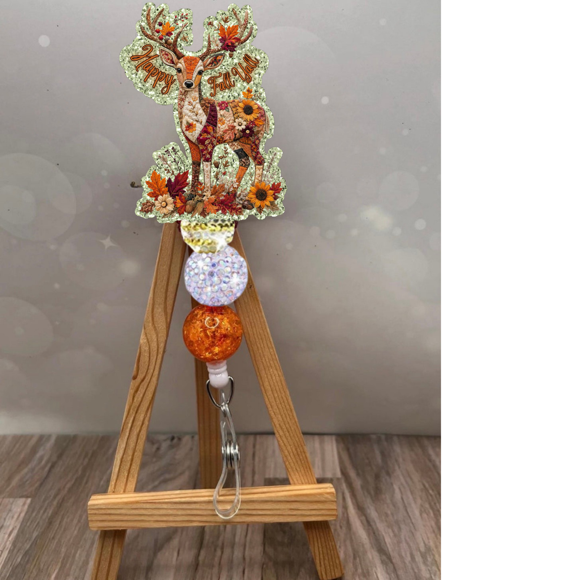 Patchwork deer badge reel featuring a glittery background and vibrant fall colors on a wooden easel display.