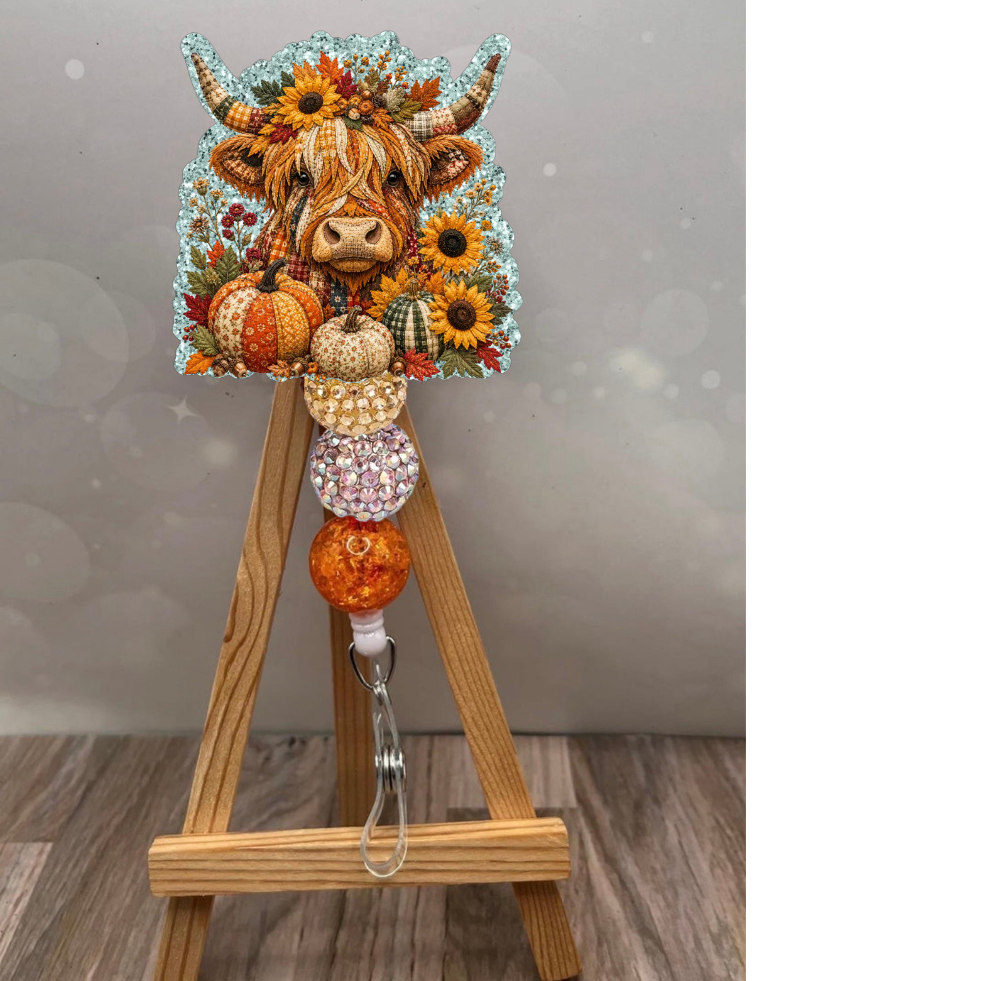 Fall Highland Cow Badge Reel featuring a fluffy Highland cow, pumpkins, and glittery beads on a wooden easel.