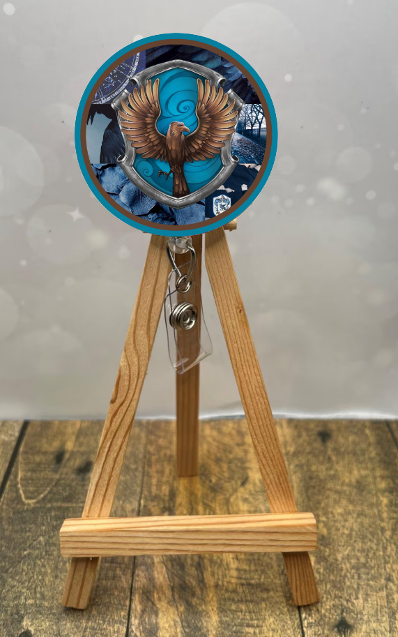 Eagle House badge pull with shimmer glitter displayed on a wooden easel with a blue and brown design.
