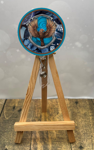 Eagle House badge pull with shimmer glitter displayed on a wooden easel with a blue and brown design.