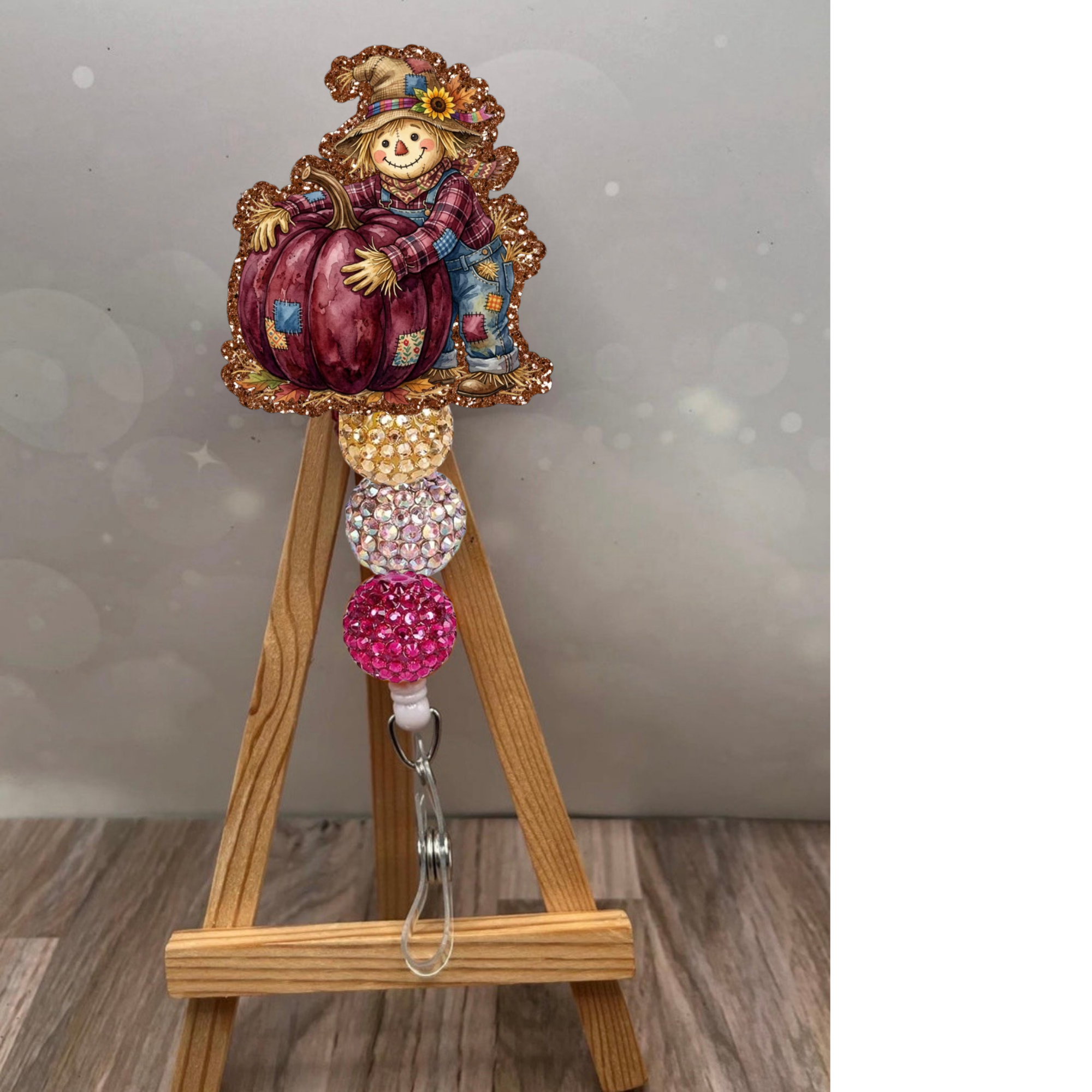 Charming scarecrow badge reel with pumpkin, featuring glitter details and fall colors for autumn-themed fun.
