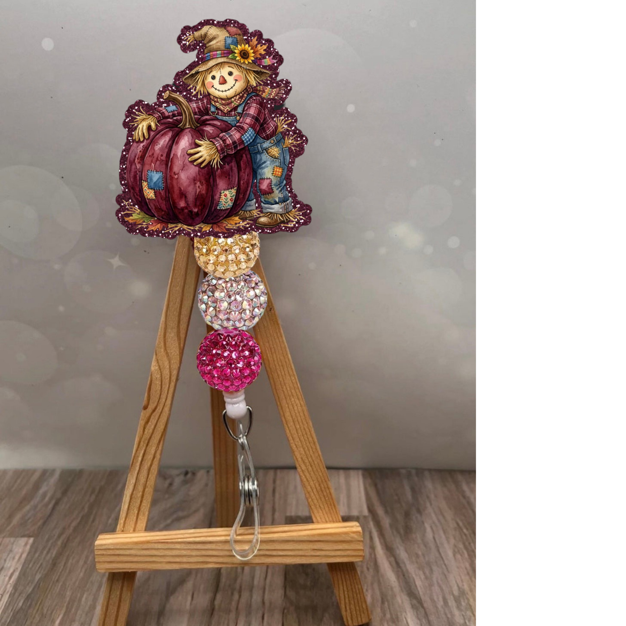 Boy scarecrow badge reel with pumpkin on a wooden easel, sparkling glitter design in plum and vibrant colors.