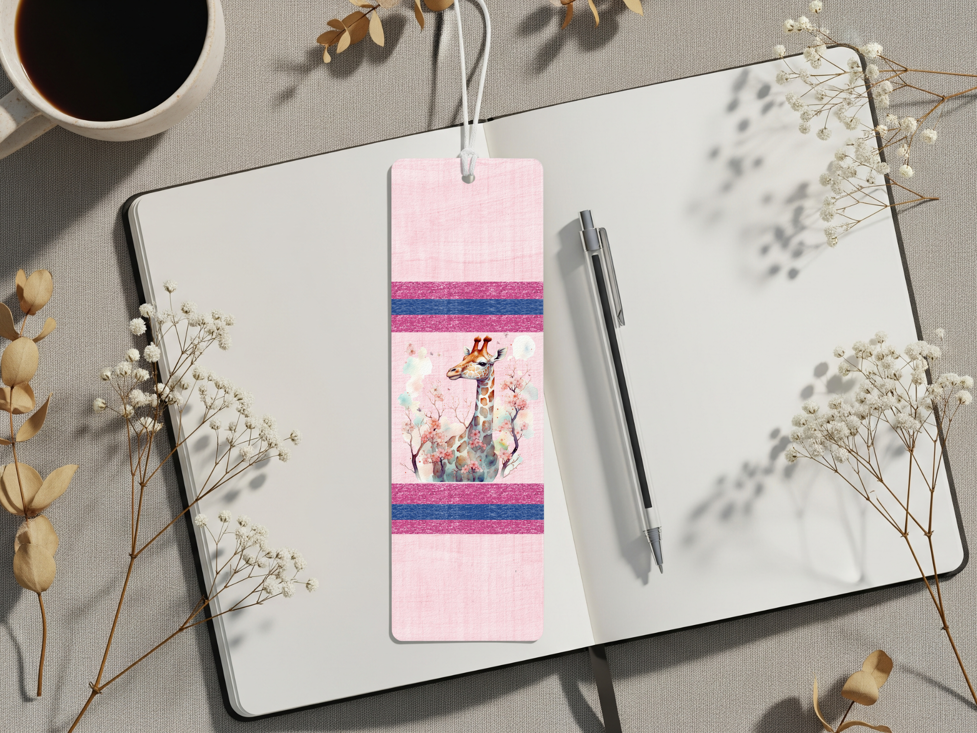 Giraffe metal bookmarks decorated with colorful artwork placed on an open notebook beside a coffee cup.