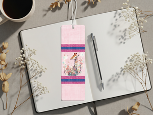 Giraffe metal bookmarks decorated with colorful artwork placed on an open notebook beside a coffee cup.