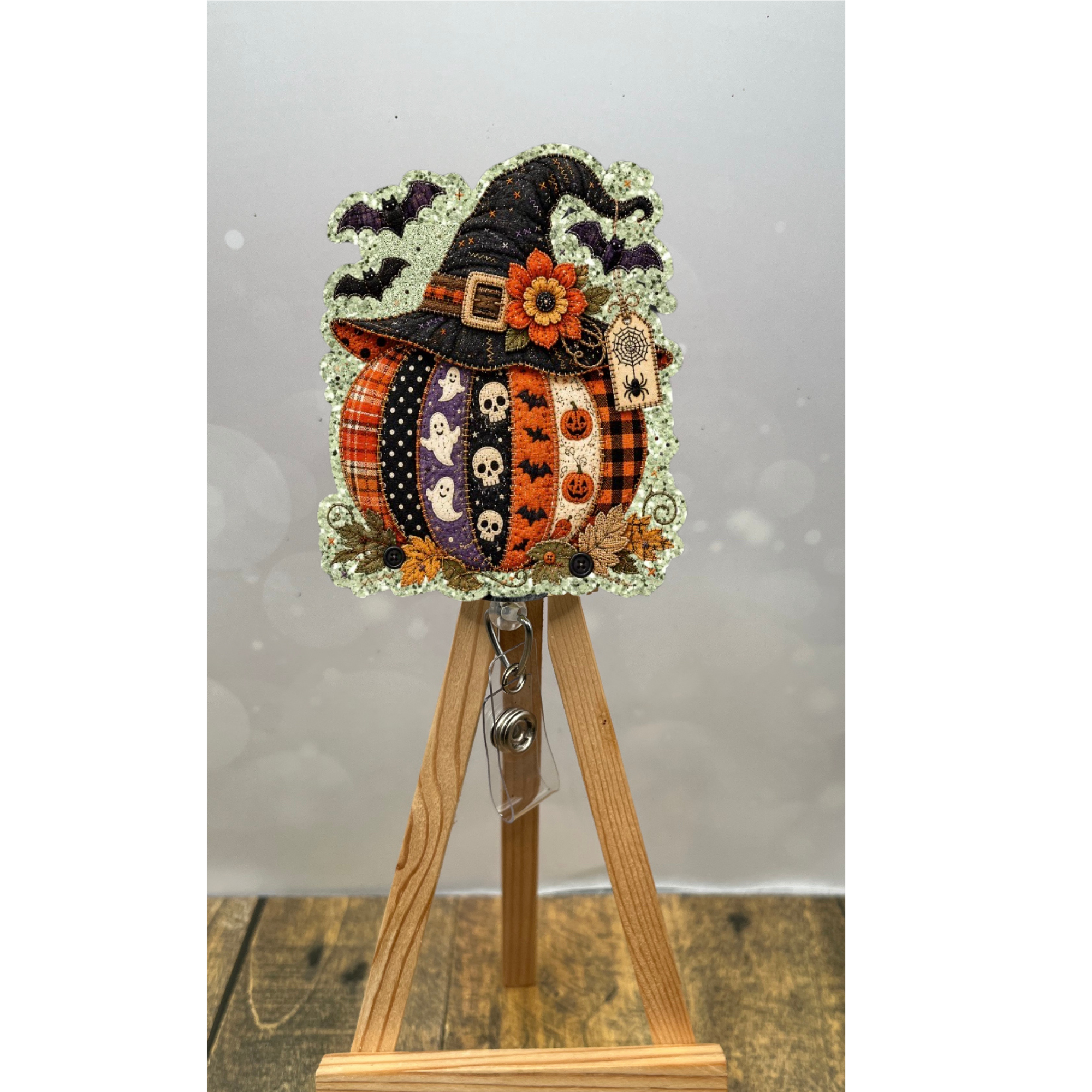 Patchwork pumpkin badge reel with glitter background and whimsical Halloween design on display.