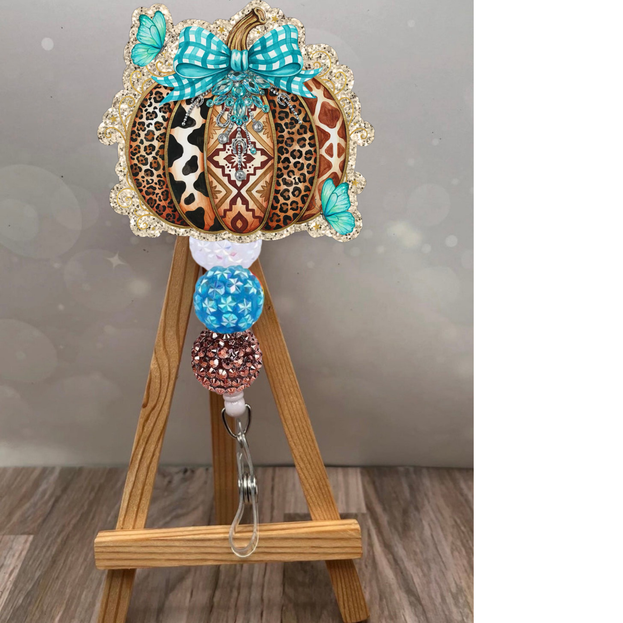 Boho pumpkin badge reel featuring a glittery pumpkin with leopard and Aztec patterns, teal bow, and colorful beads.