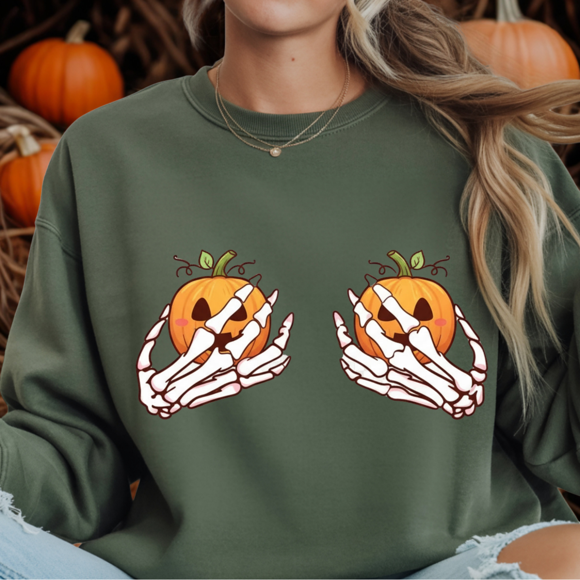 A person wearing an olive green sweatshirt with a Halloween graphic of skeleton hands holding orange jack-o'-lantern pumpkins. The background is filled with pumpkins.