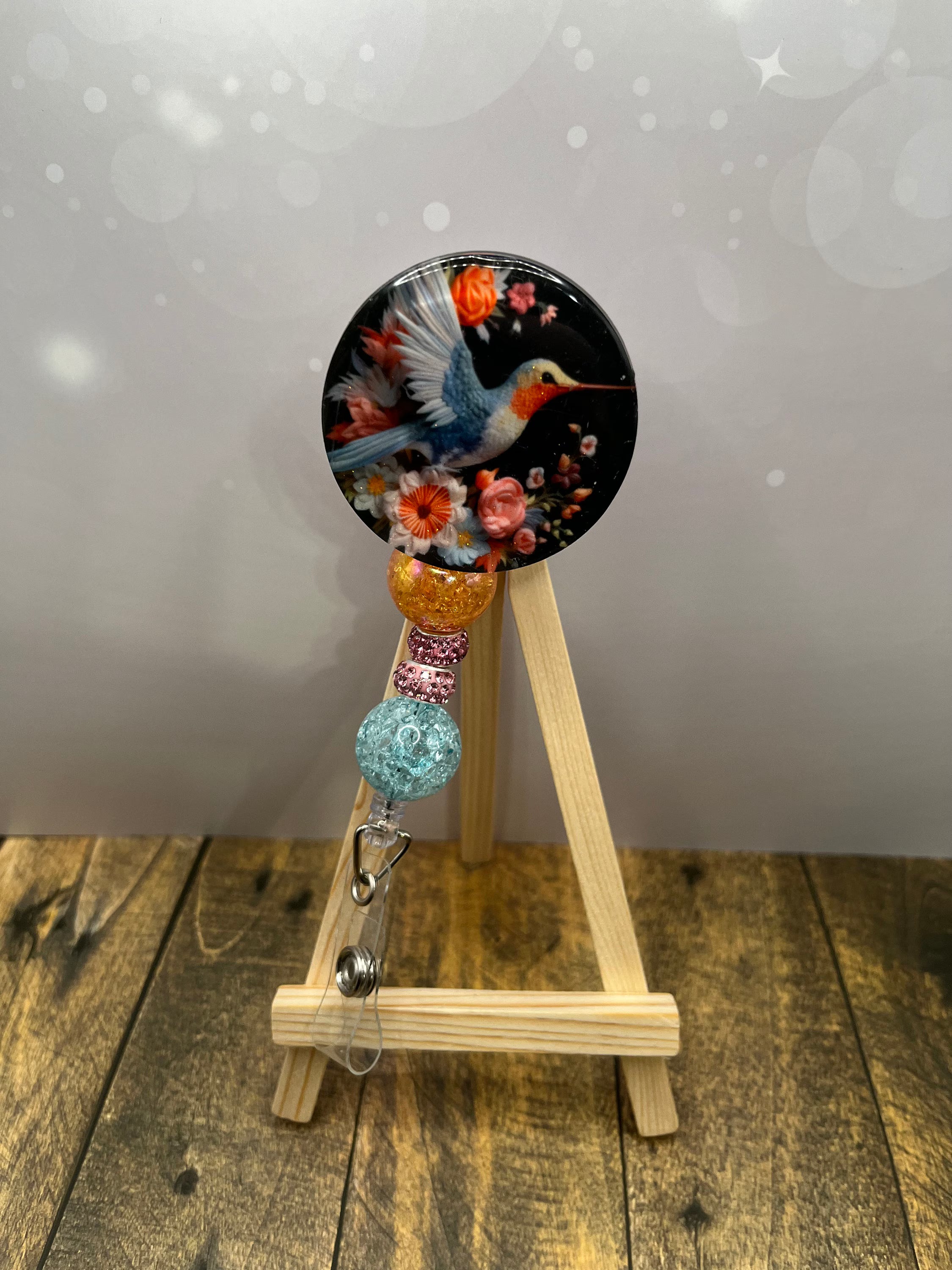 Hummingbird badge pulls featuring a colorful design with flowers and bead accents on a reel.