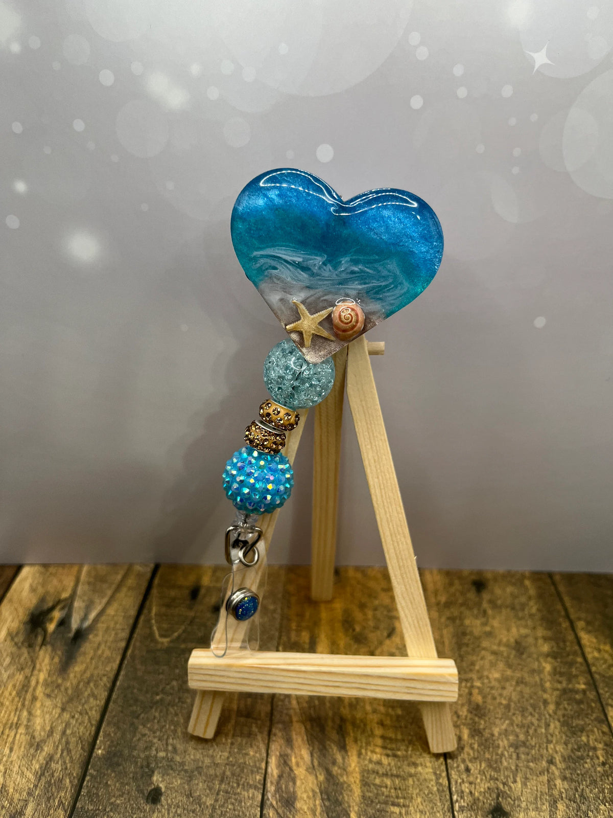 Blue heart-shaped object with beads on a wooden stand against a gray background