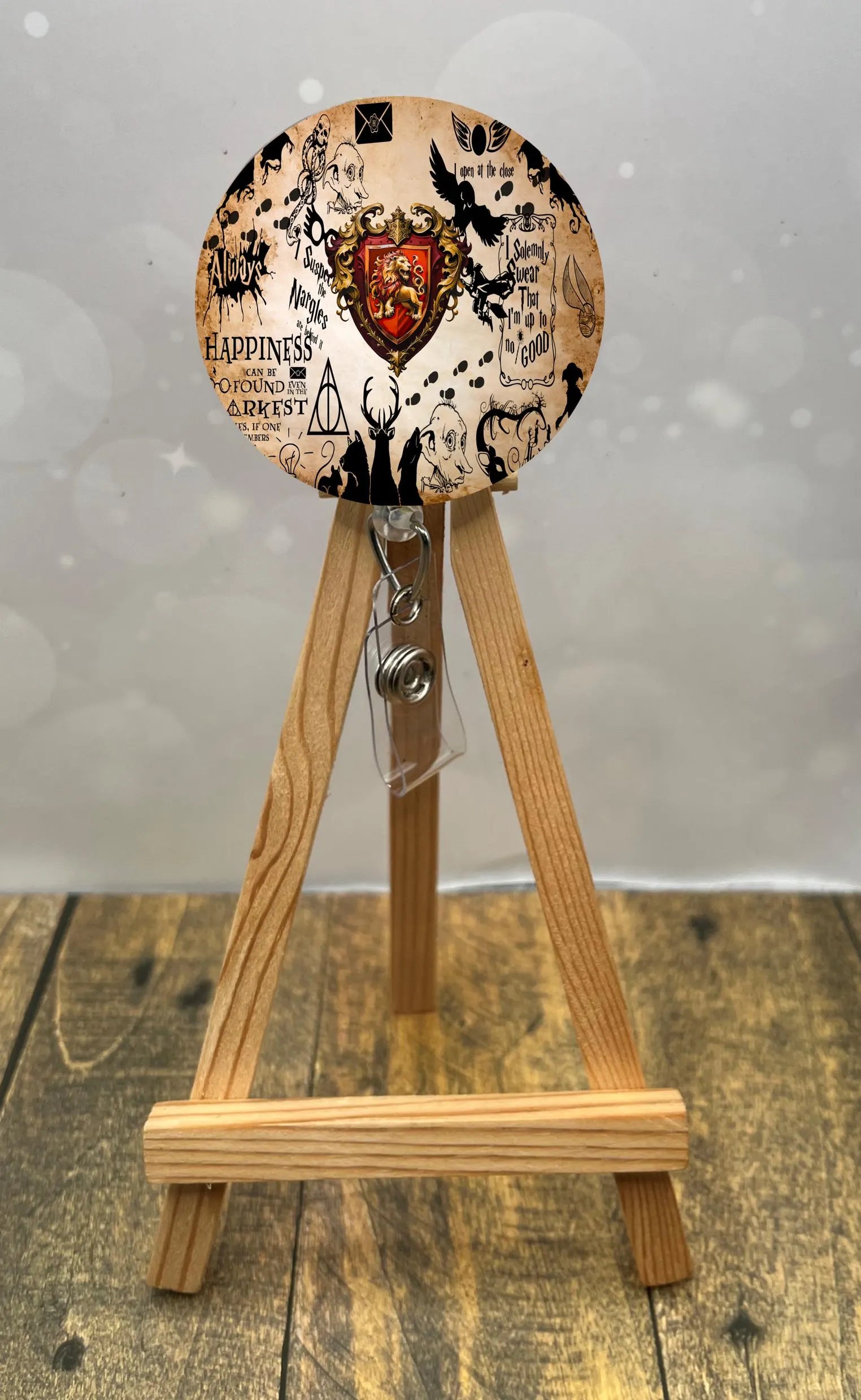 Gryffindor badge pull with glitter displayed on an easel, featuring vibrant colors and magical design elements.