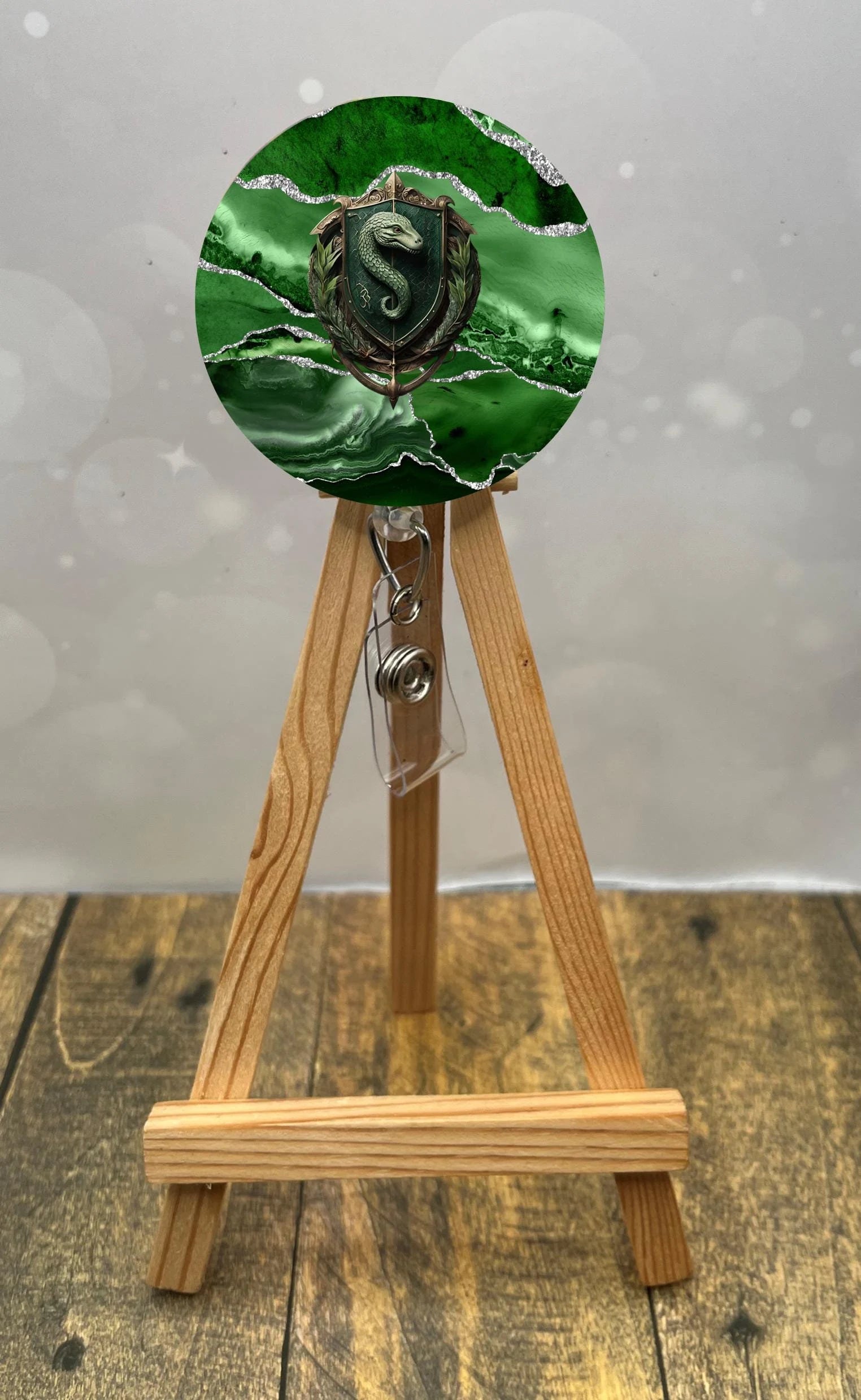 Slytherin badge pull with glitter displayed on a wooden easel, featuring green and black marble design.