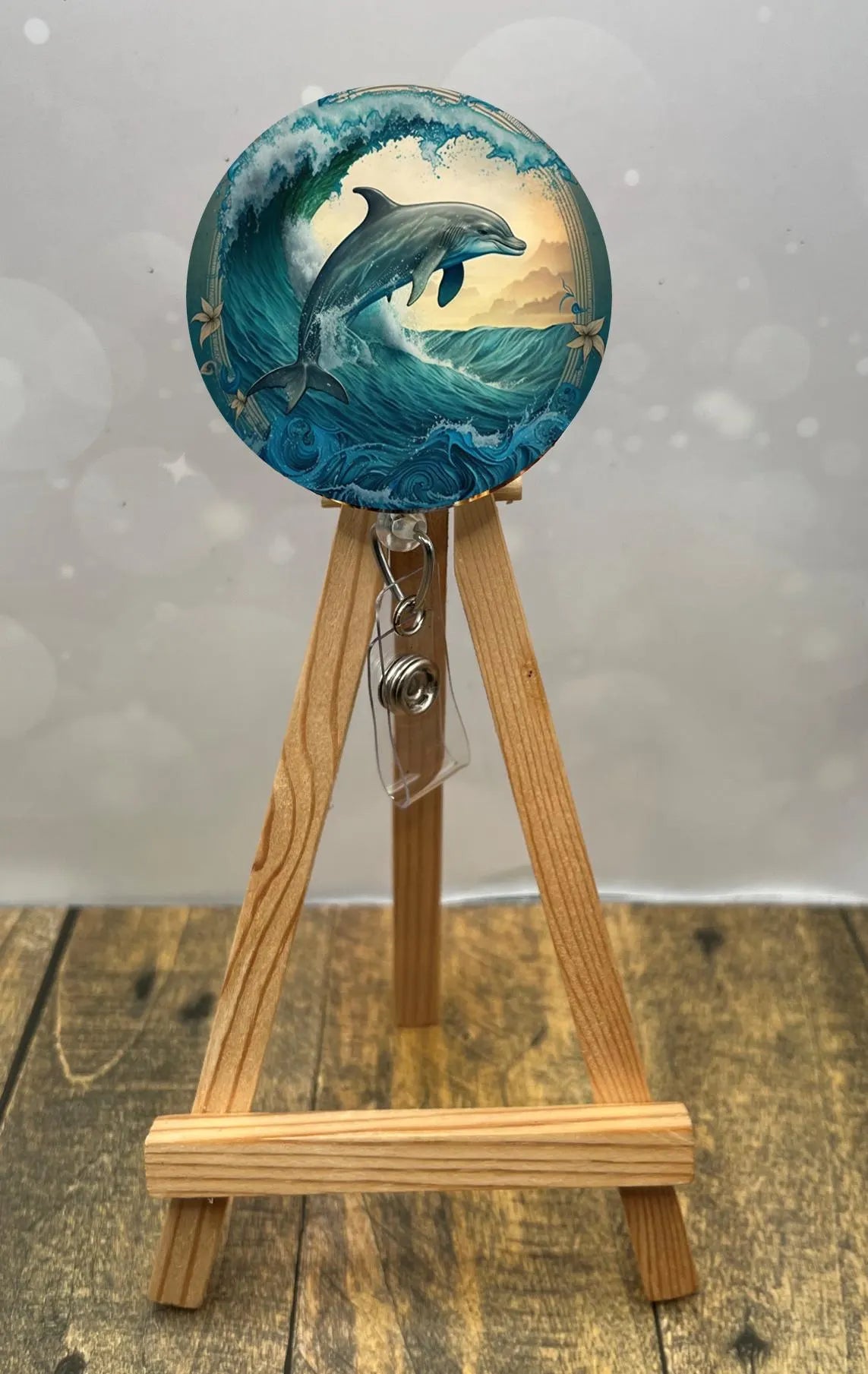 Dolphin badge pull with glitter featuring playful dolphin artwork on a retractable reel, displayed on a wooden easel.