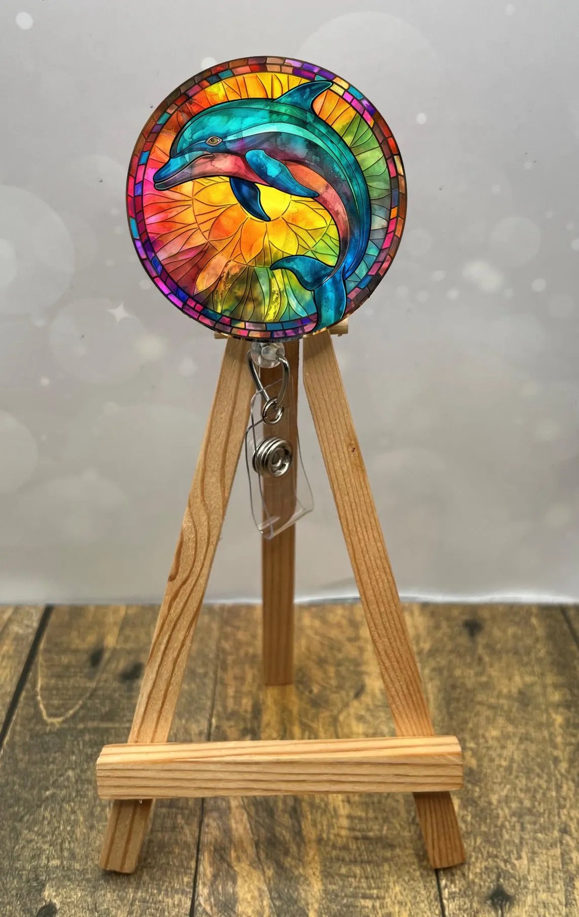Colorful dolphin badge pull with glitter, showcasing vibrant artwork on a wooden display stand.