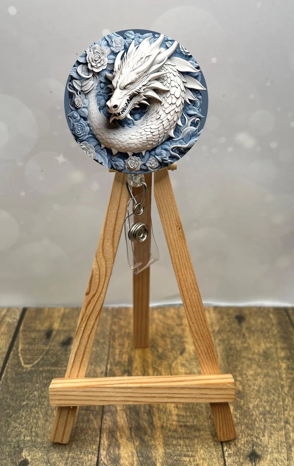 Dragon badge pull reel featuring a detailed dragon design surrounded by blue roses on an easel display.