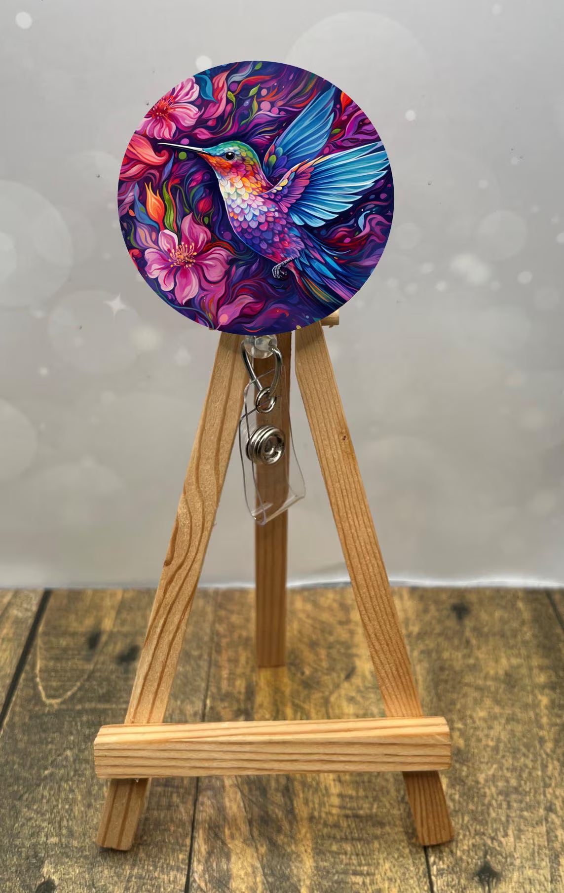 Hummingbird badge pulls displayed on a wooden easel, featuring vibrant floral design and colorful hummingbird.