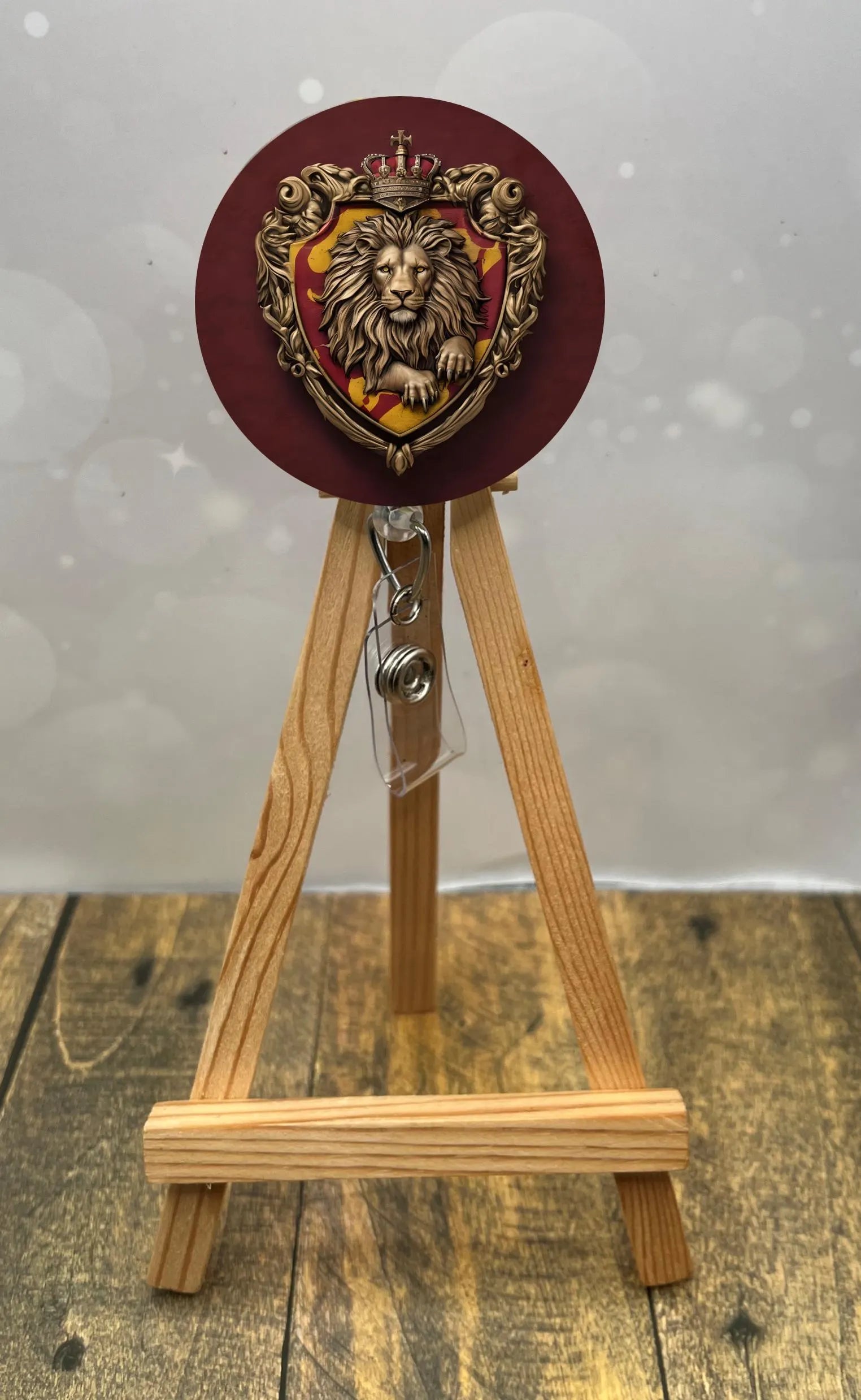 Gryffindor badge pull with glitter displayed on a wooden easel, featuring a lion crest design.