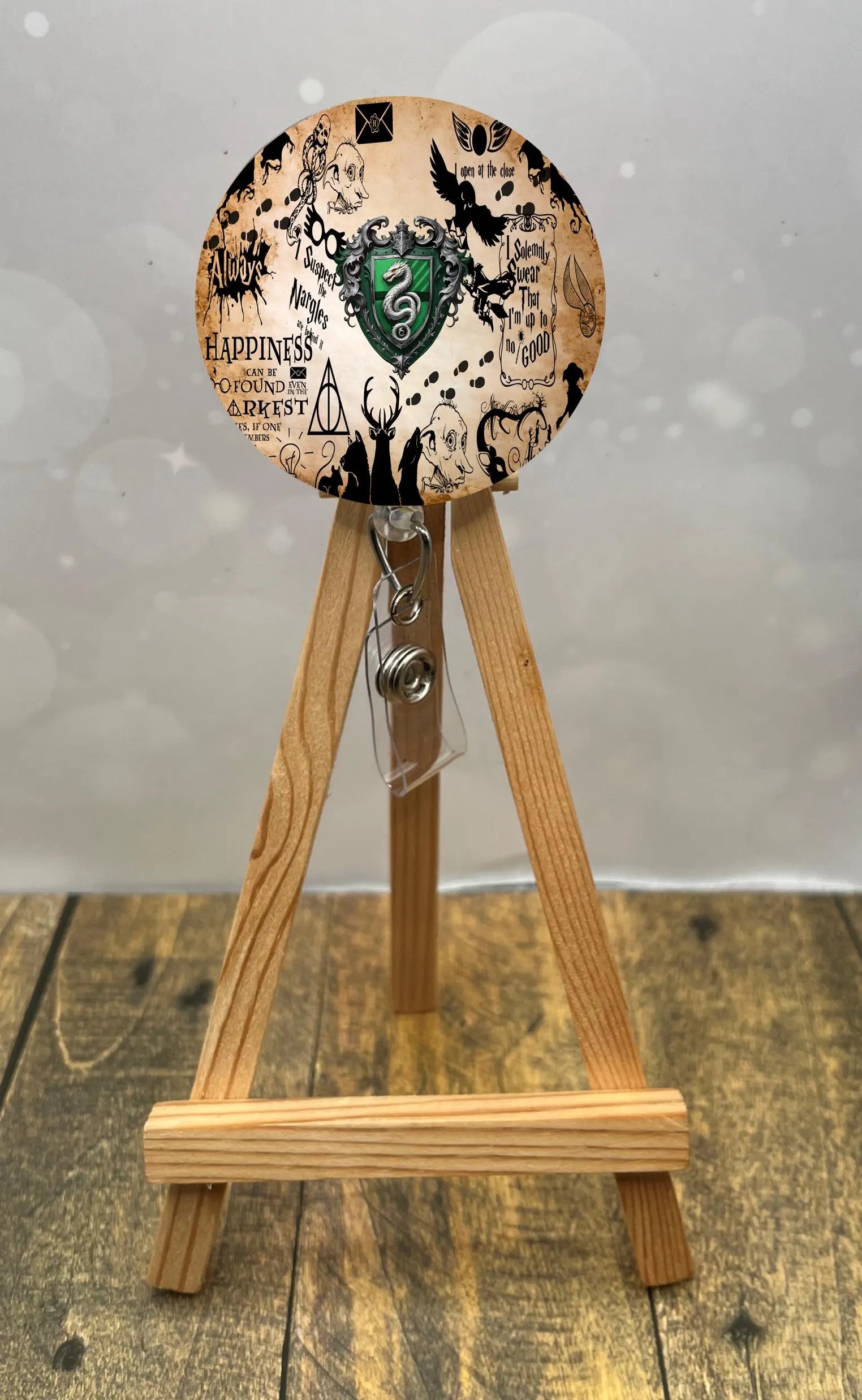 Slytherin badge pull with glitter displayed on a wooden stand featuring magical designs.
