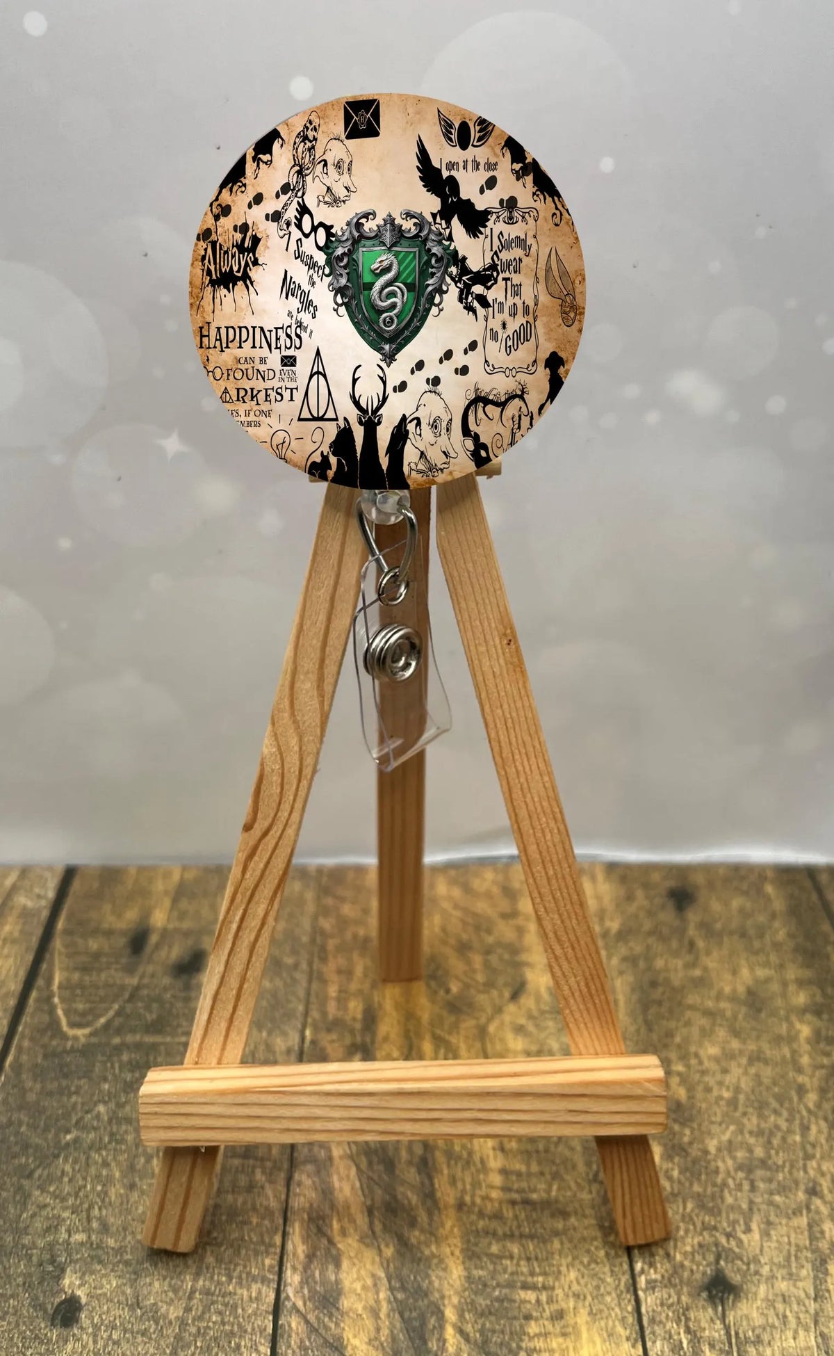 Slytherin badge pull with glitter displayed on a wooden stand featuring magical designs.