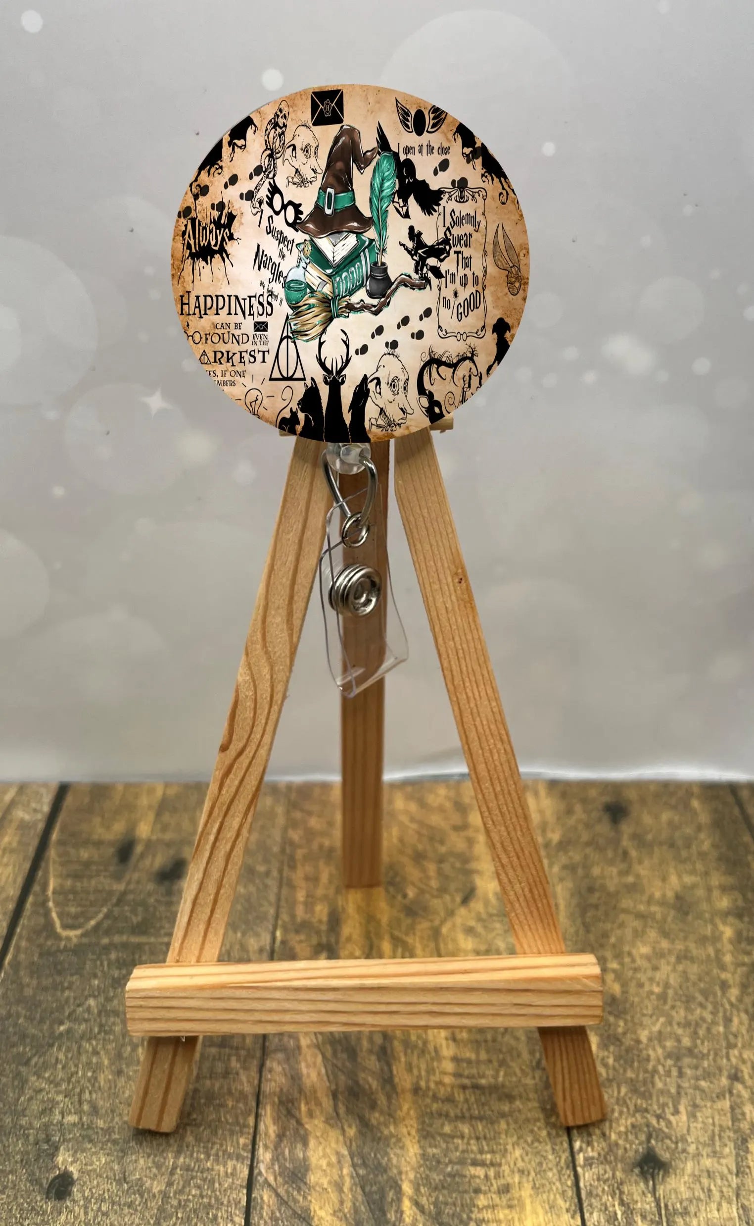 Slytherin badge pull with glitter displayed on wooden easel, featuring colorful design and retractable clip.