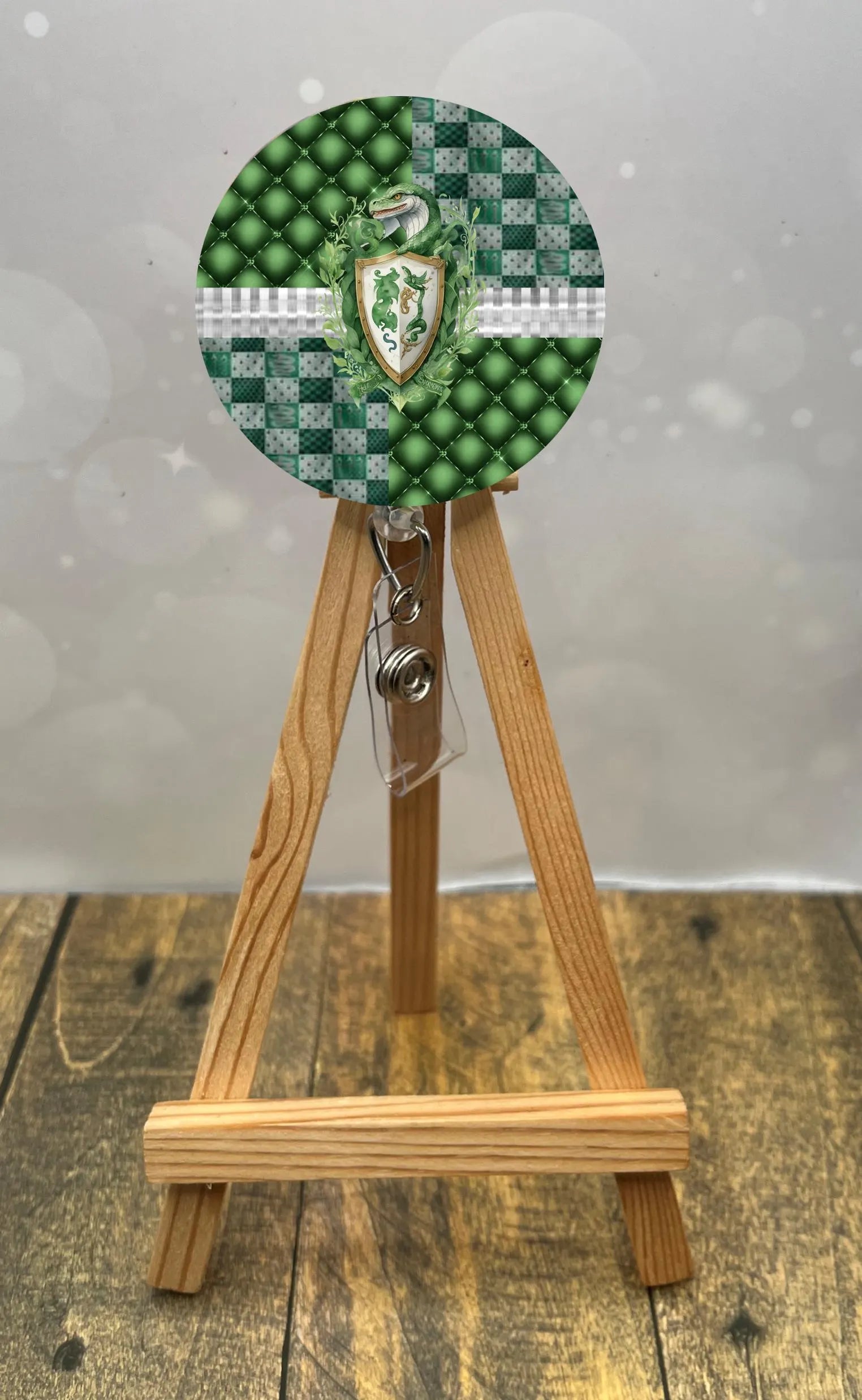 Slytherin badge pull with glitter displayed on wooden easel, featuring green beads and shield design.