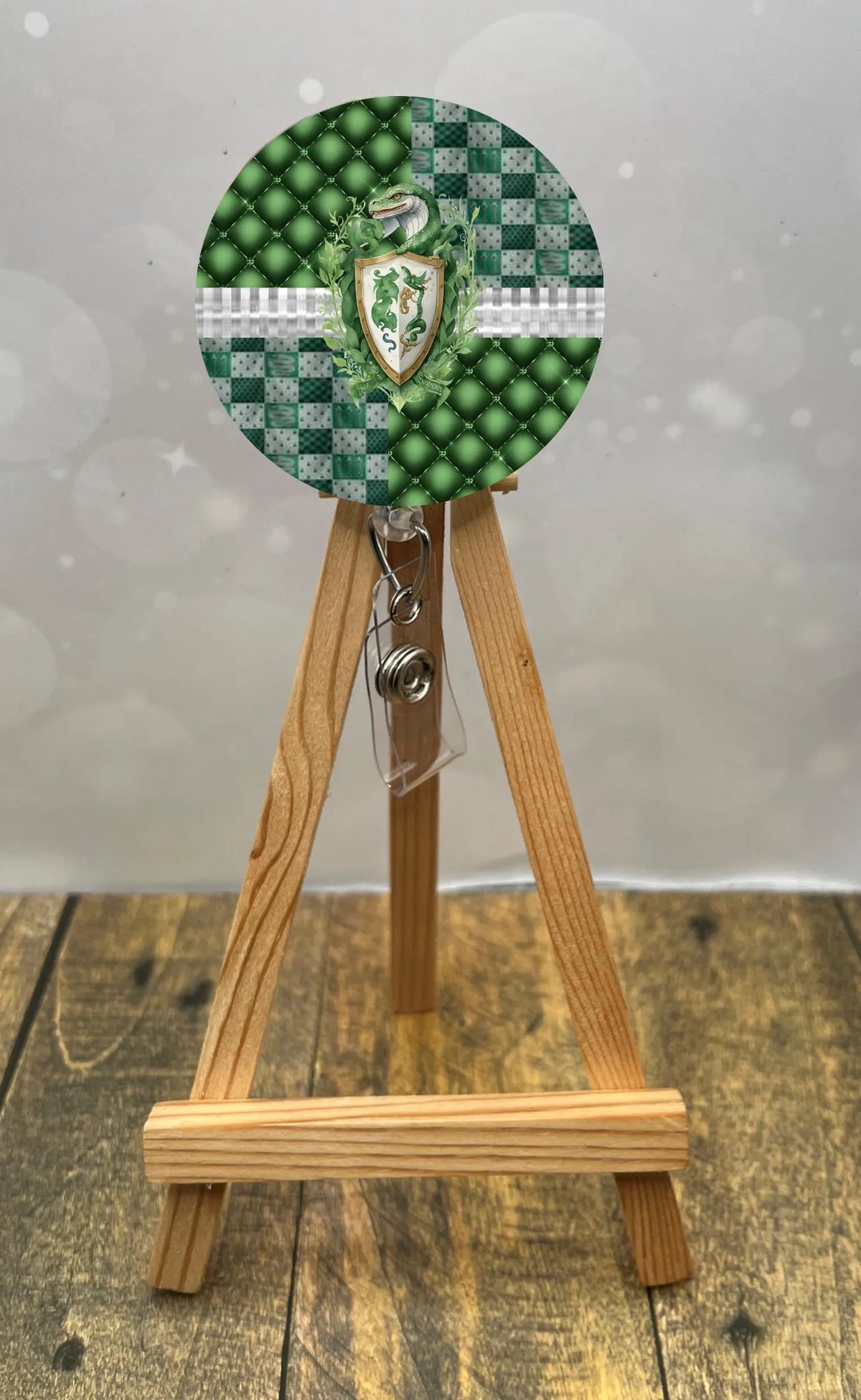 Slytherin badge pull with glitter displayed on wooden easel, featuring green beads and shield design.