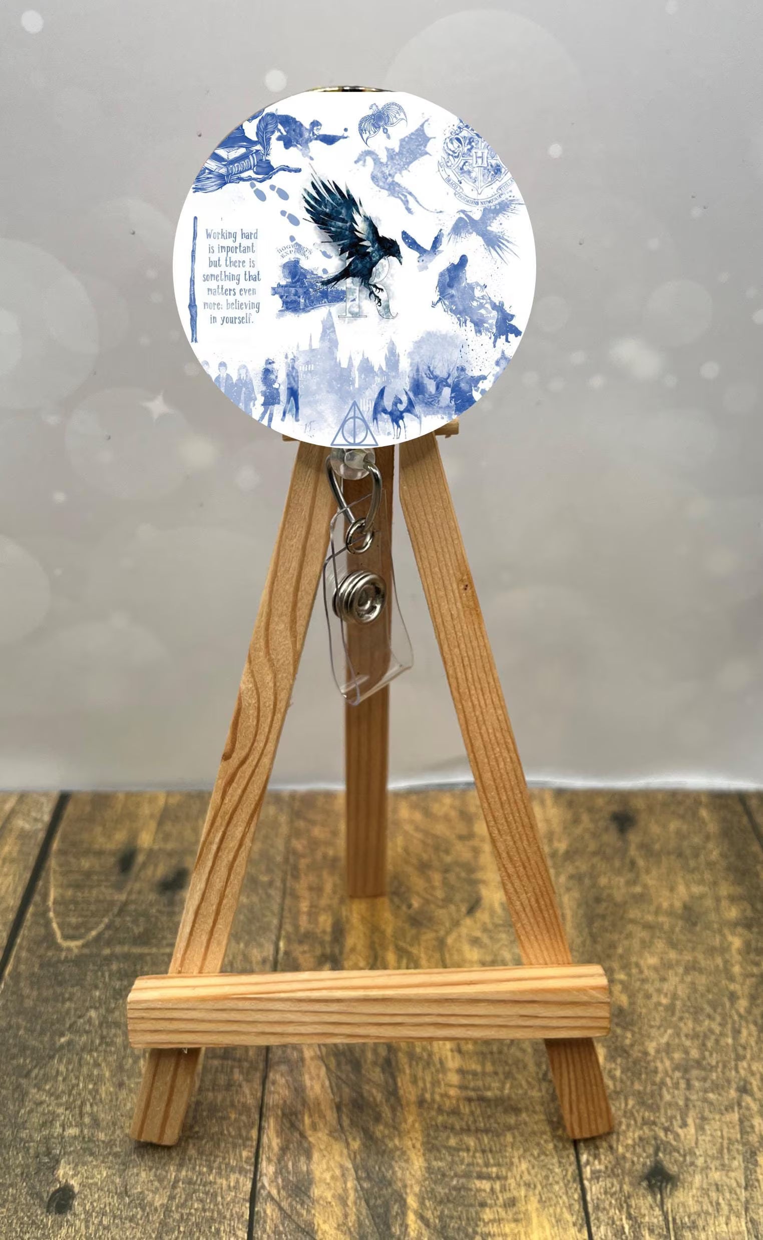 Eagle House badge pull with shimmer glitter displayed on an easel, featuring blue-themed illustrations and a retractable clip.