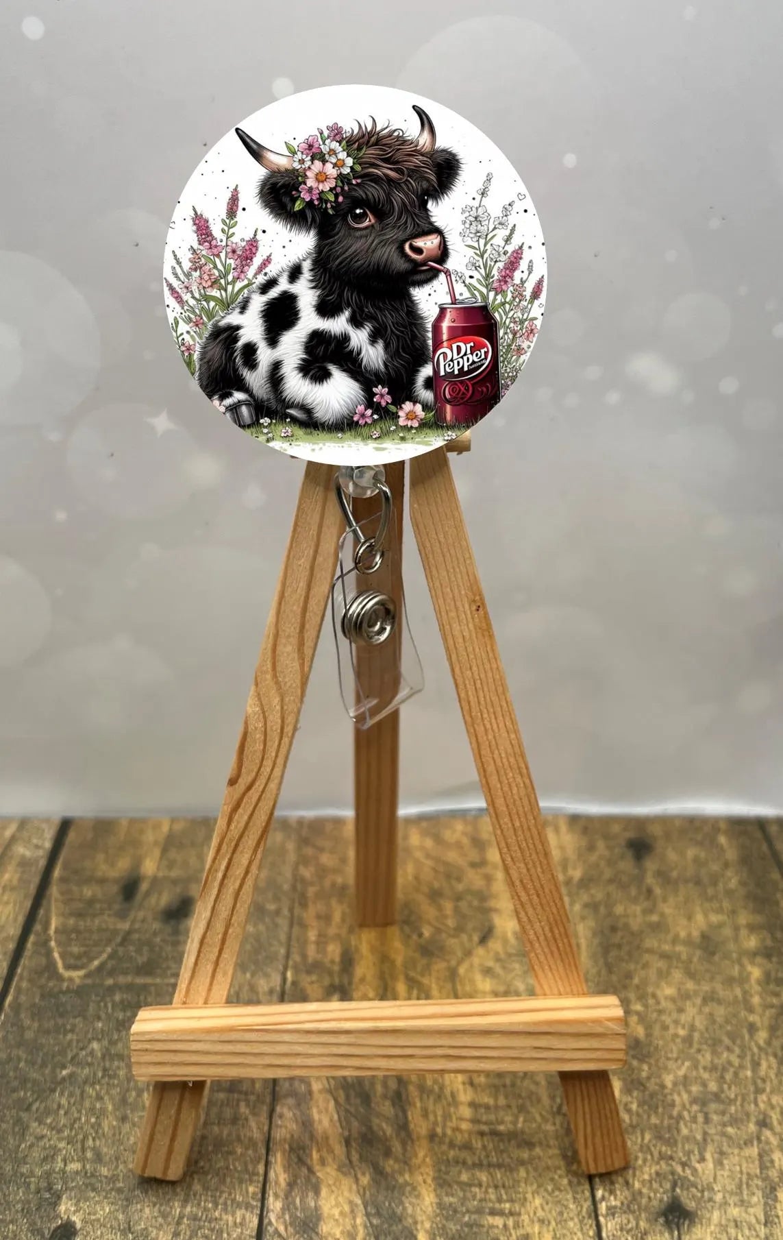 Highland cow badge pull featuring a cute cow design with flowers and a Dr Pepper can on an easel.