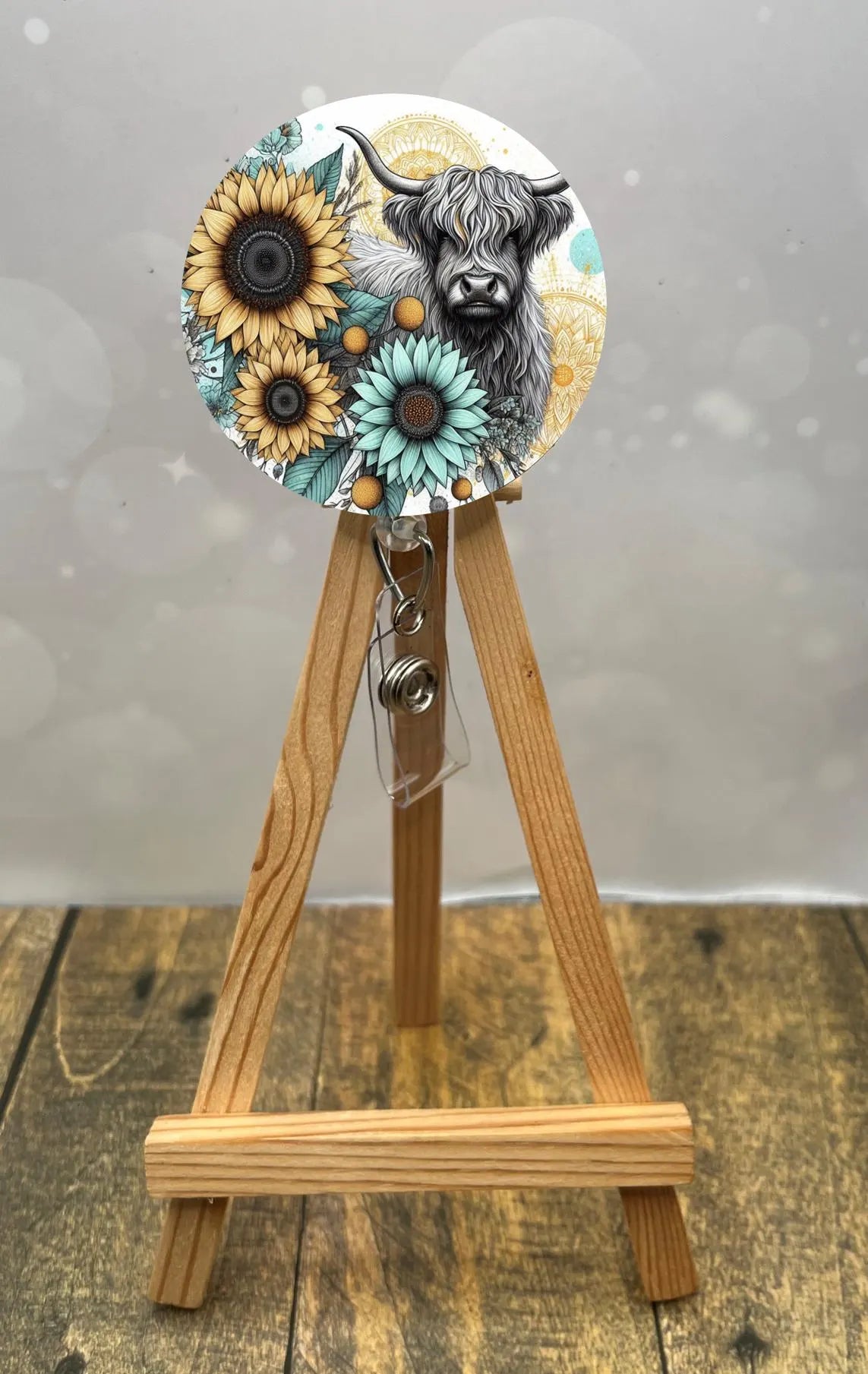 Highland cow badge pull with sunflower design on a wooden easel, adding charm to any workday.