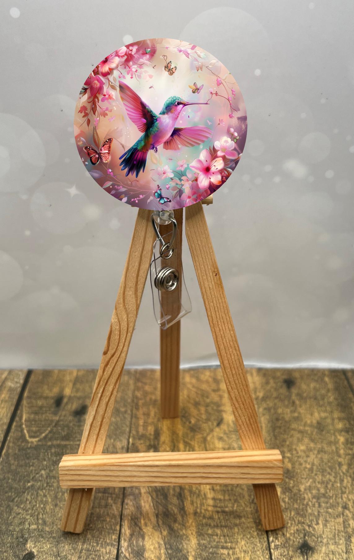 Hummingbird badge pulls with vibrant colors on a wooden easel, floral details and butterflies, perfect for brightening your workday.